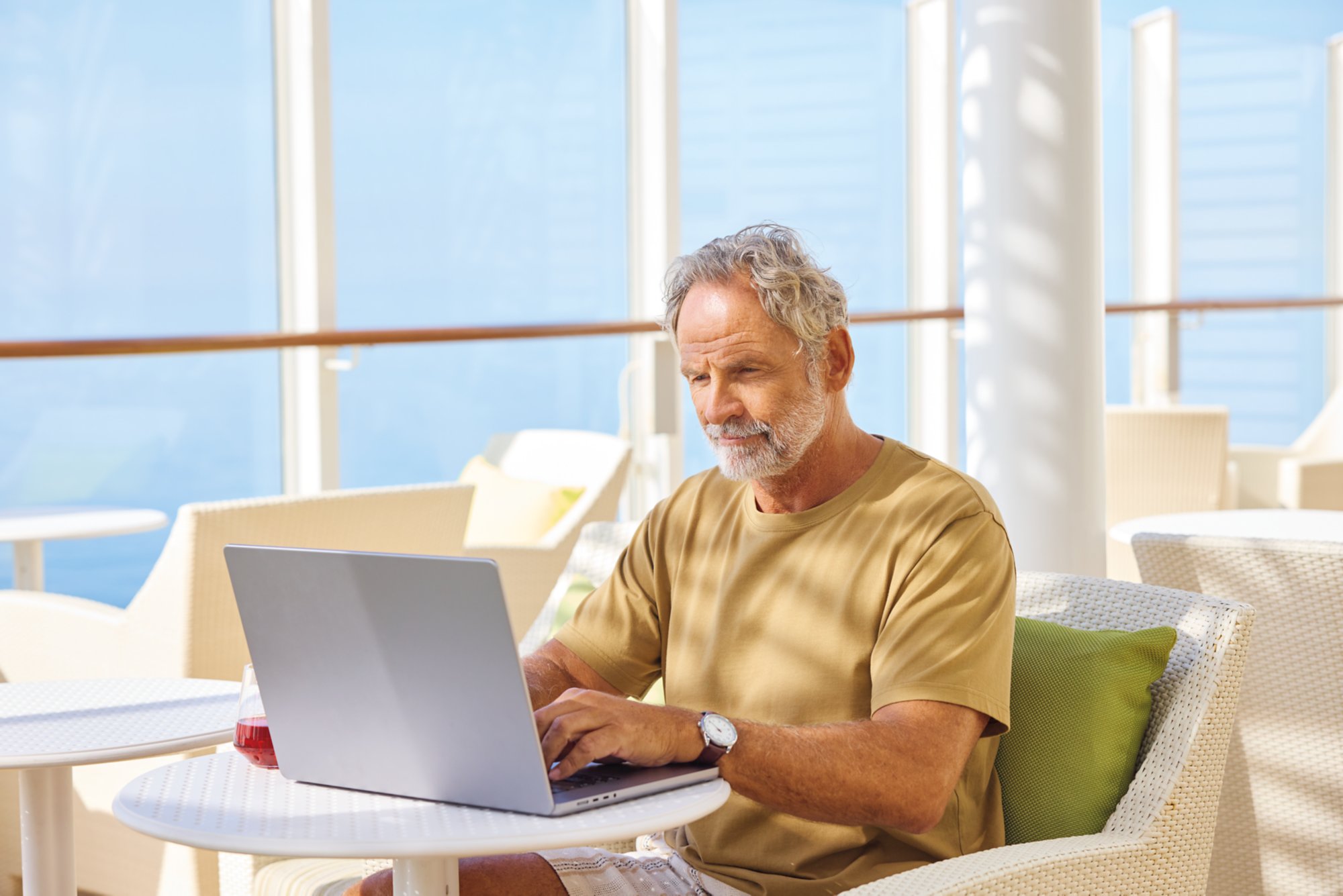 Ein älterer Herr sitzt an einem Tisch an Deck vor einem Laptop
