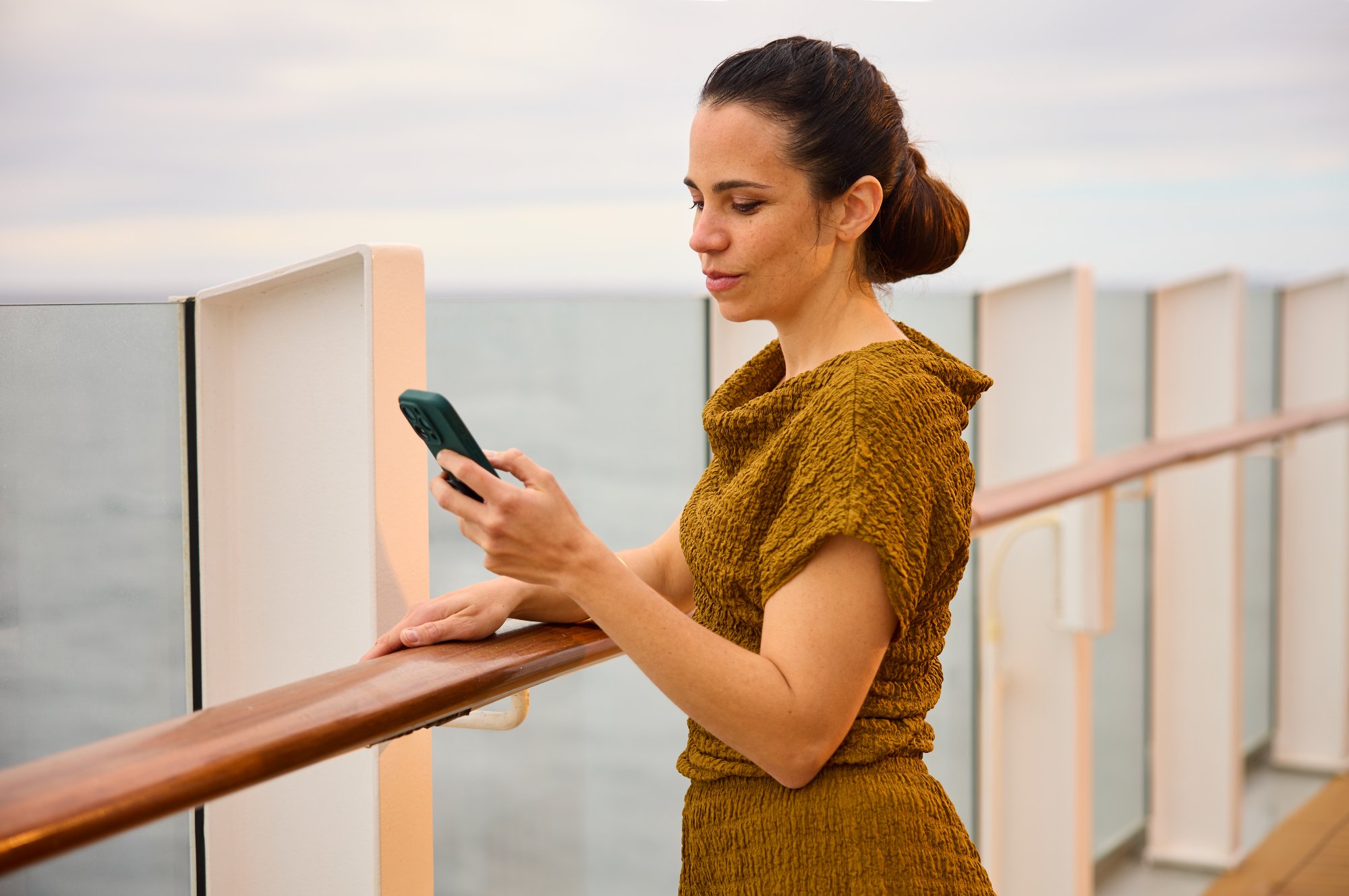 Frau mit einem Smartphone in der Hand. Steht an der Reling.