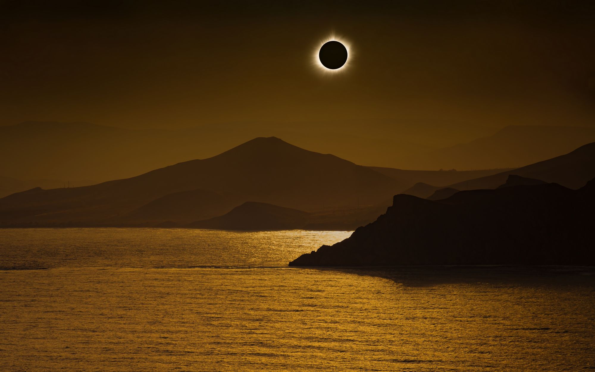 Totale Sonnenfinsternis am dunkelroten Himmel über Bergen und Meer. 