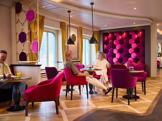 French Kiss Bar mit magentafarbenen Stühlen, runden Wandmustern und großen Fenstern.