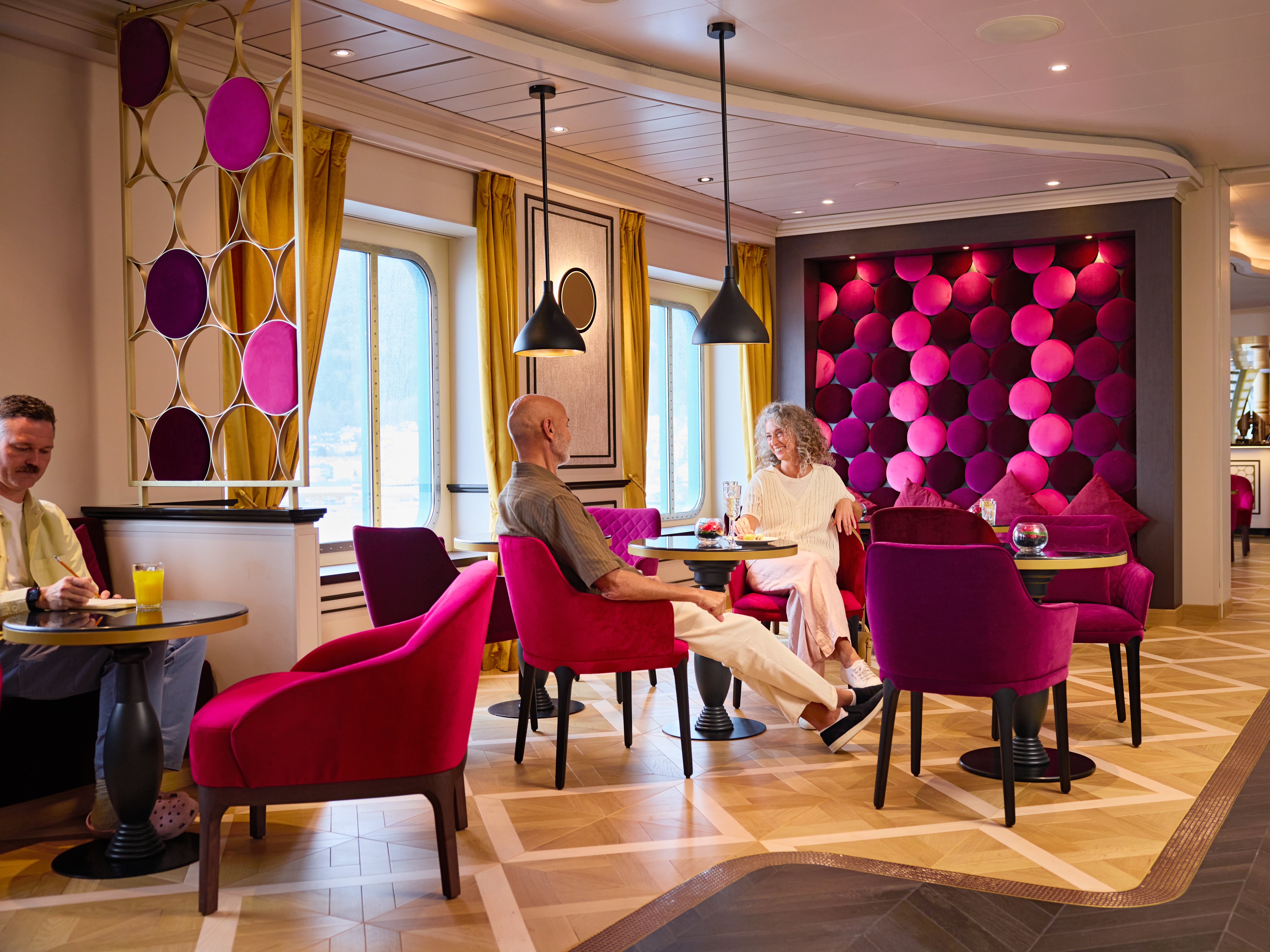 French Kiss Bar mit magentafarbenen Stühlen, runden Wandmustern und großen Fenstern.