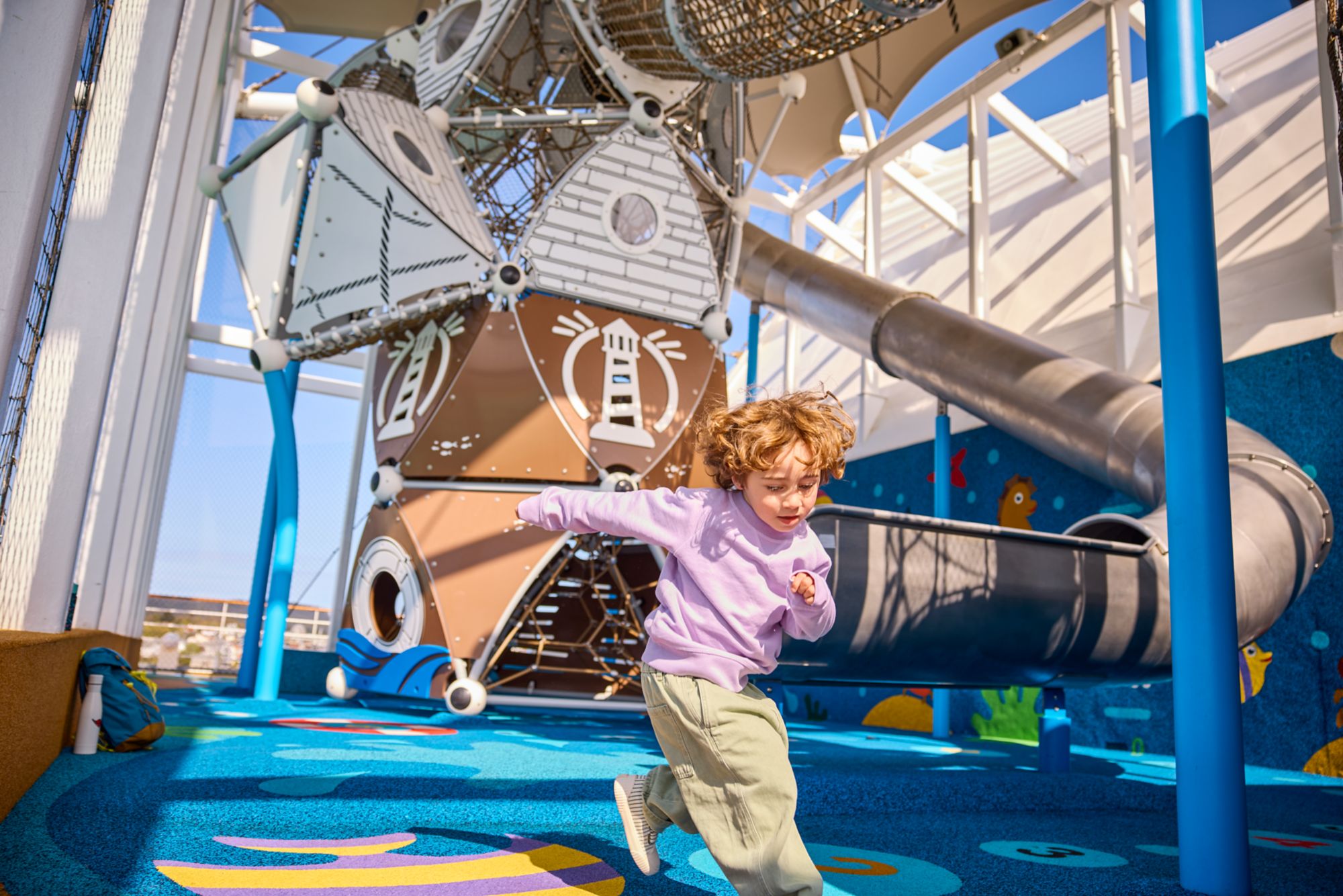 Kind läuft in einem Indoor-Spielplatz mit Kletterstruktur und buntem Boden.