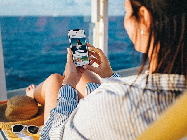 Frau mit Smartphone sitzt auf dem Außendeck