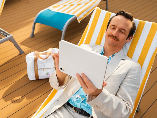 Ein Mann auf einer Sonnenliege hält ein Tablet in der Hand und tippt darauf