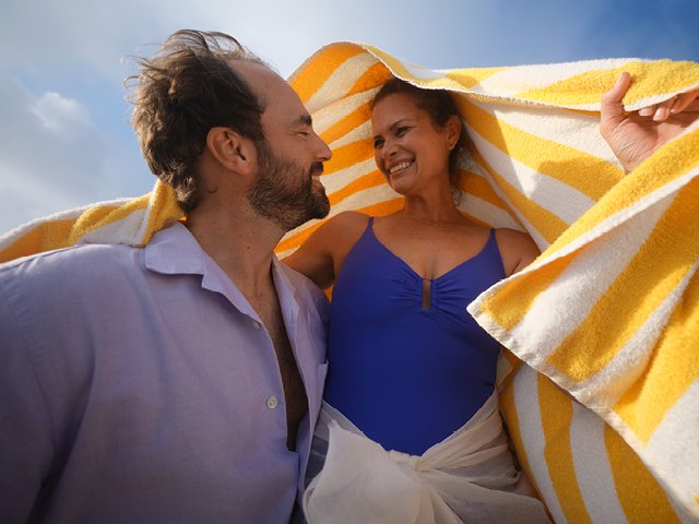 Ein Pärchen umarmt sich, sie breitet ein Handtuch wie ein Zelt über den beiden aus