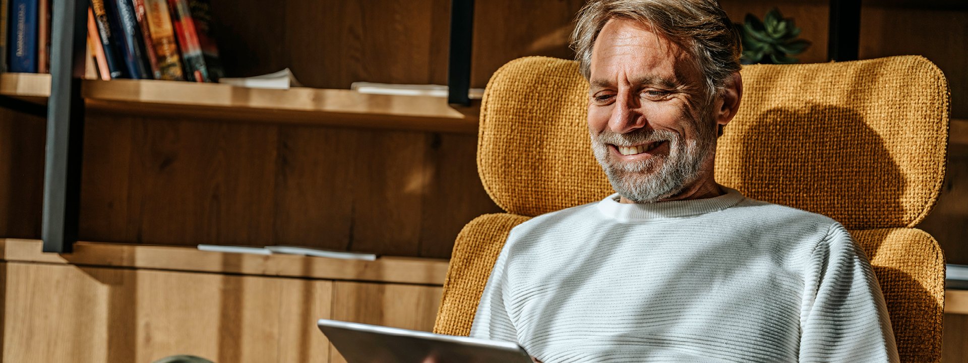 Ein Mann sitzt auf einem Sessel und blickt auf sein Tablet, das er in den Händen hält