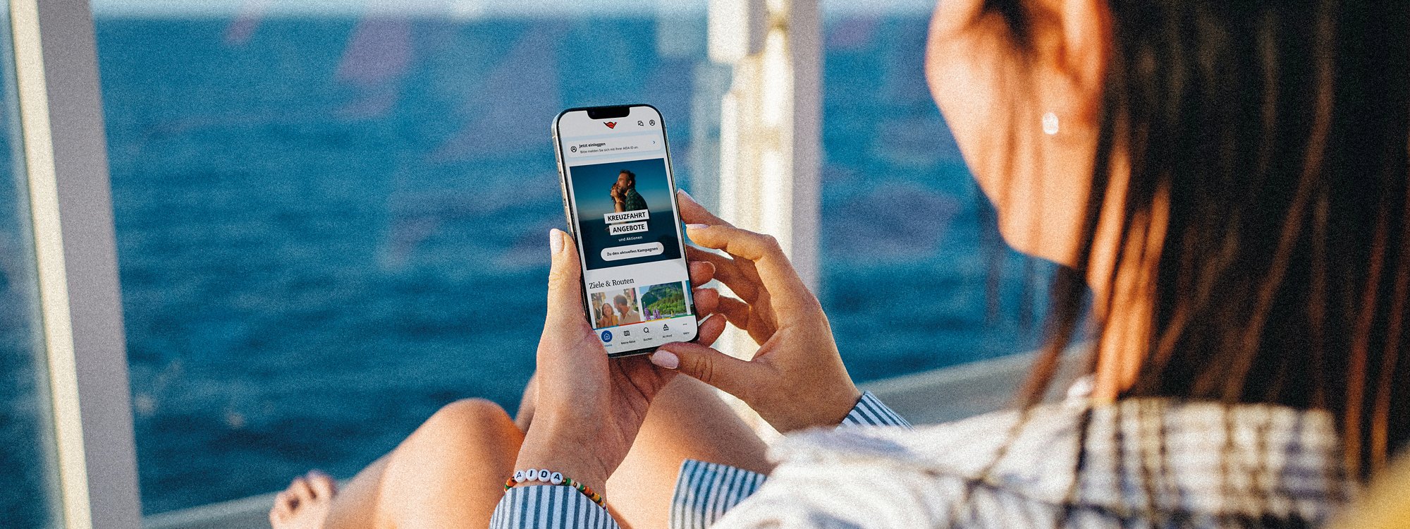 Blick über die Schulter einer Frau, die auf einer Liege sitzt und auf ihr Smartphone schaut