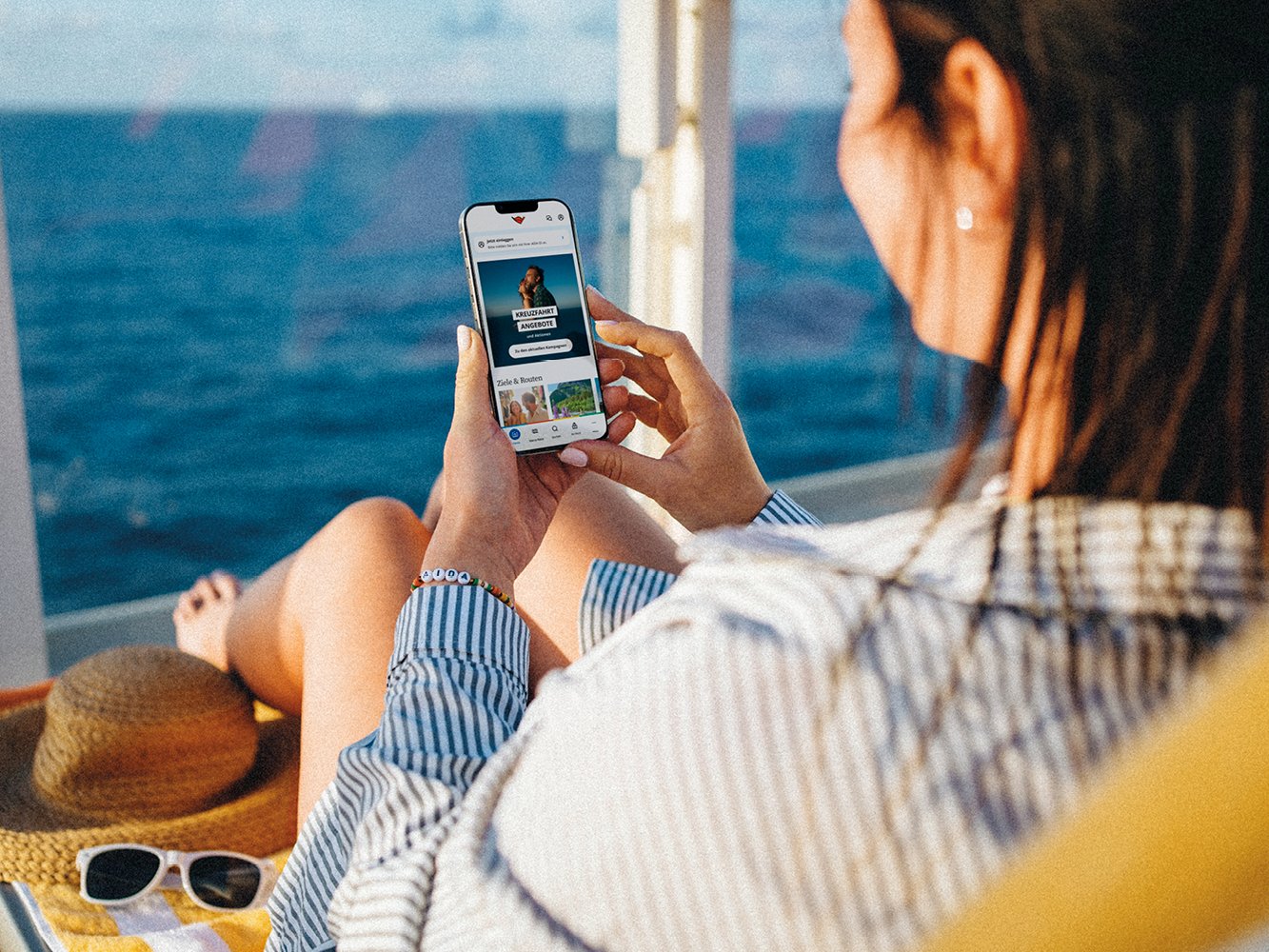 Blick über die Schulter einer Frau, die auf einer Liege sitzt und auf ihr Smartphone schaut
