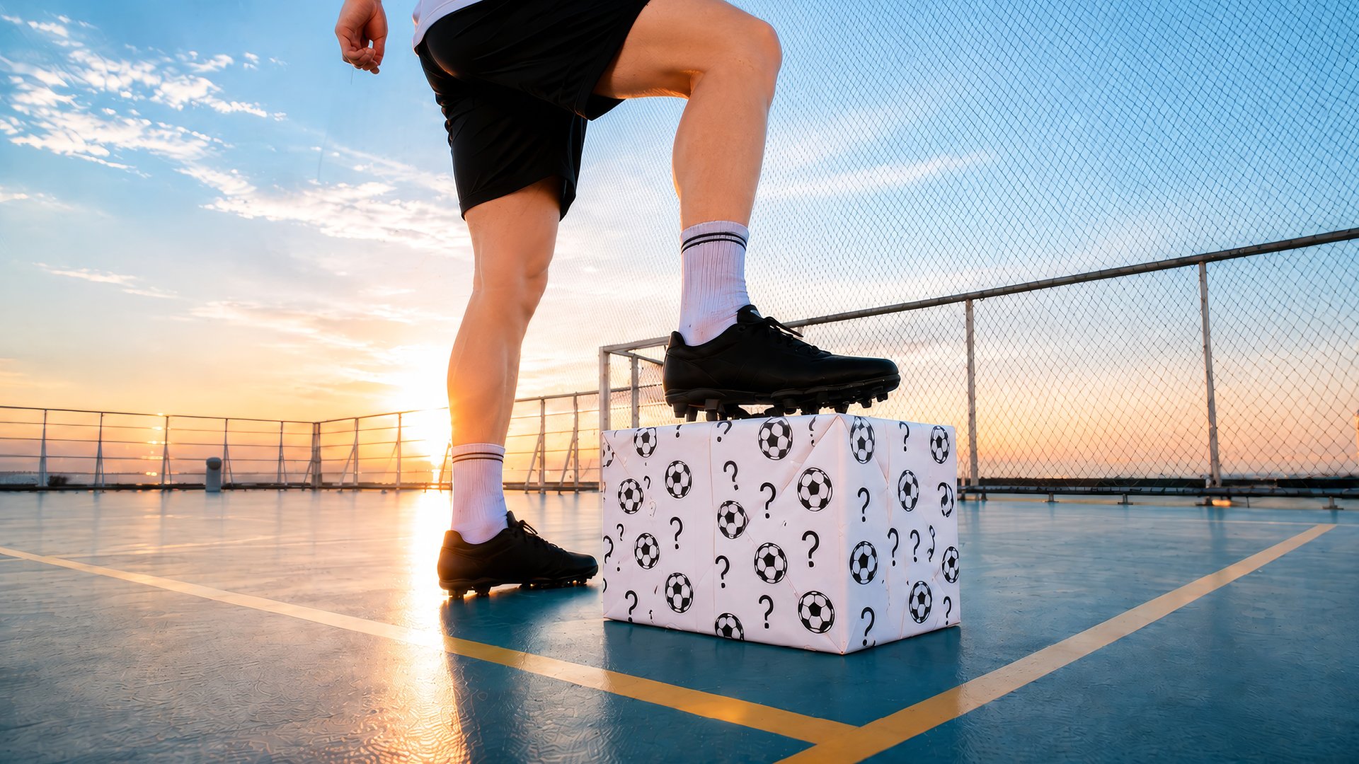 Eine Person steht an Deck, hat Fußballschuhe an und stht mit einem Fuß auf einem Paket mit Fragezeichen und Fußballsymbolen