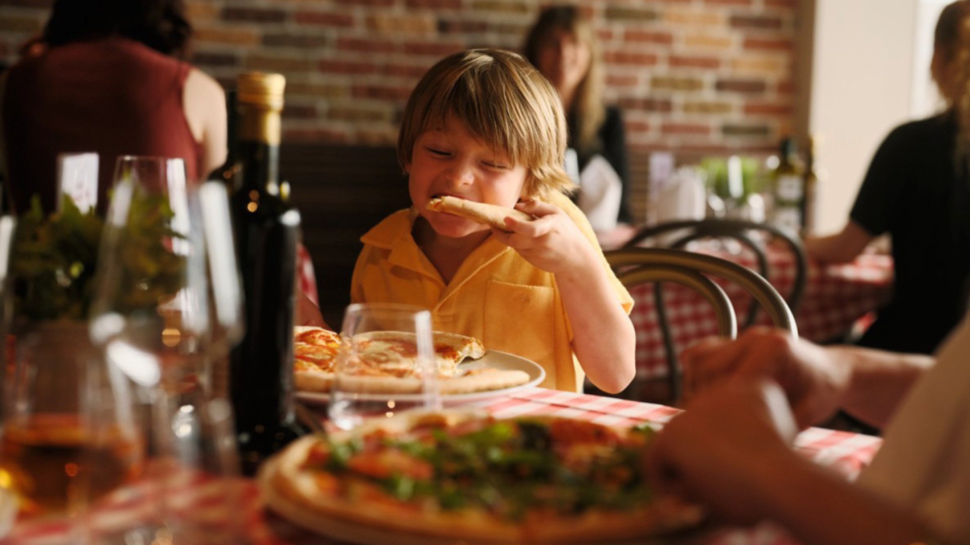 Kleiner Junge sitzt im Restaurant an Bord und beißt genüsslich in ein Stück Pizza