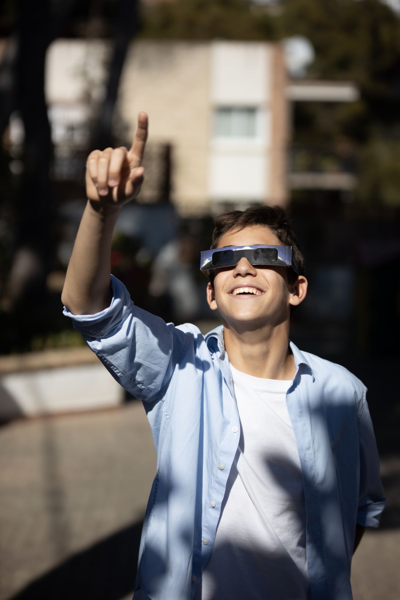 Ein lächelnder Teenager betrachtet eine Sonnenfinsternis mit Sonnensichtbrille und zeigt nach oben