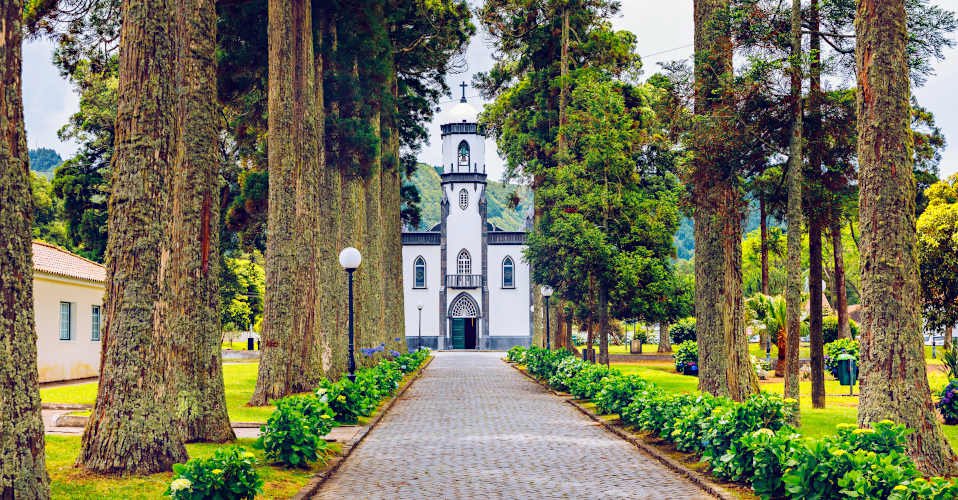 Church of Sao Nicolau (Saint Nicolas) with an alley of tall trees and hydrangea flowers in Sete cidades on Sao Miguel island, Azores, Portugal. Parish Church of St. Nicholas, Sete Cidades, Azores.