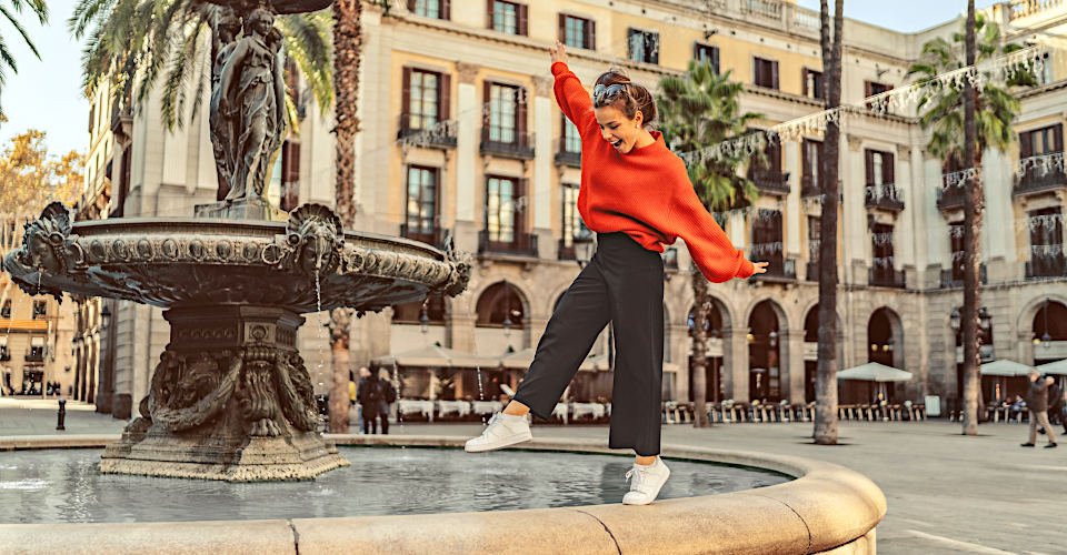 Smiling woman trying to keep balance while walking on one leg at the fountain