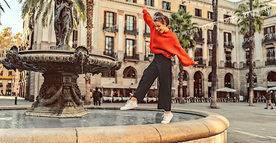 Smiling woman trying to keep balance while walking on one leg at the fountain