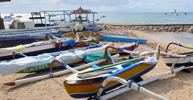 TOUR OPERATOR GATEWAY - Traditional fishing boats rest on the sandy shore of Sanur Beach.