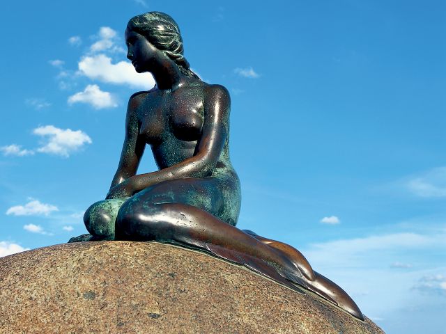 Die Statue der kleinen Meerjungfrau sitzt auf einem Felsen vor blauem Himmel in Kopenhagen, Dänemark.