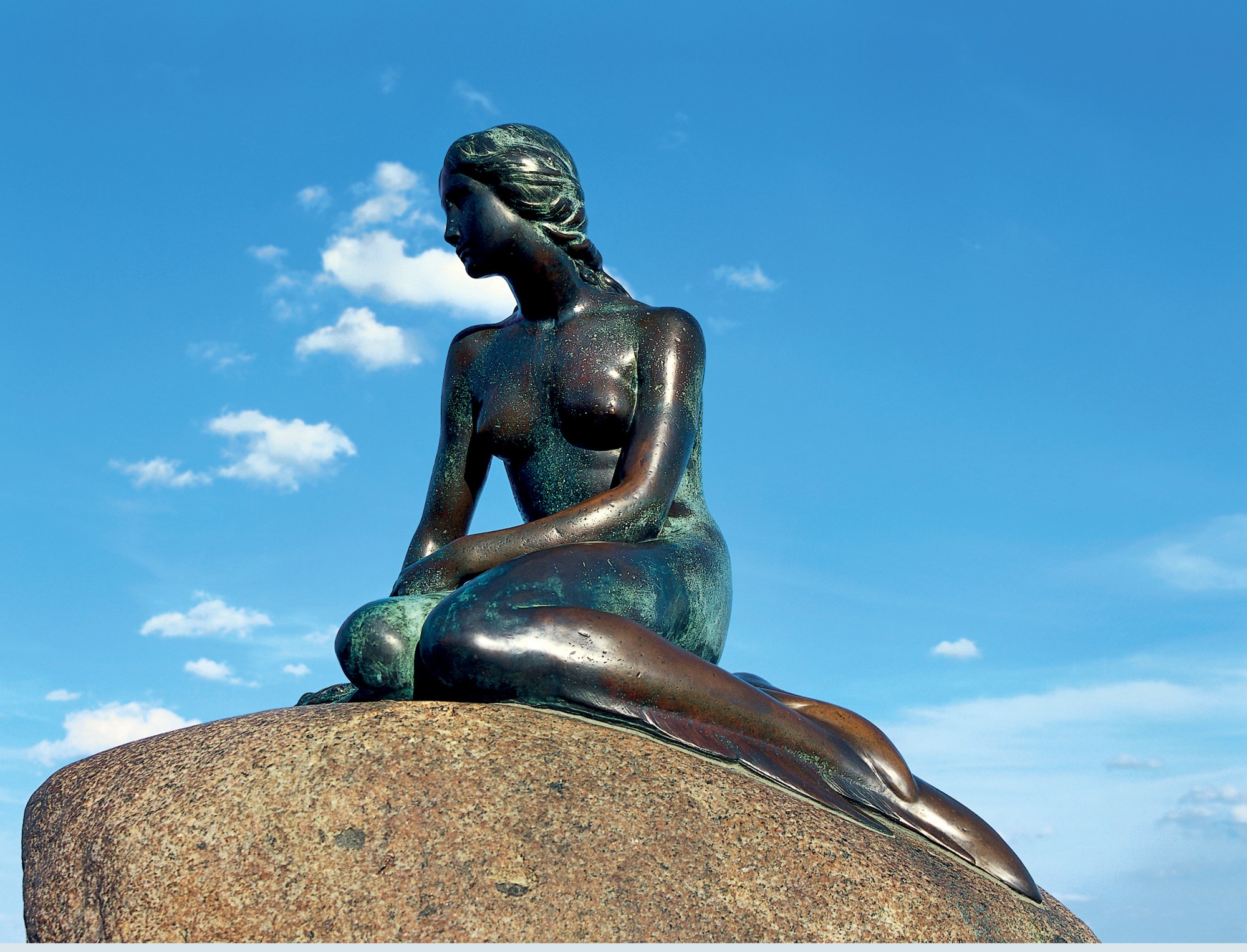 Die Statue der kleinen Meerjungfrau sitzt auf einem Felsen vor blauem Himmel in Kopenhagen, Dänemark.
