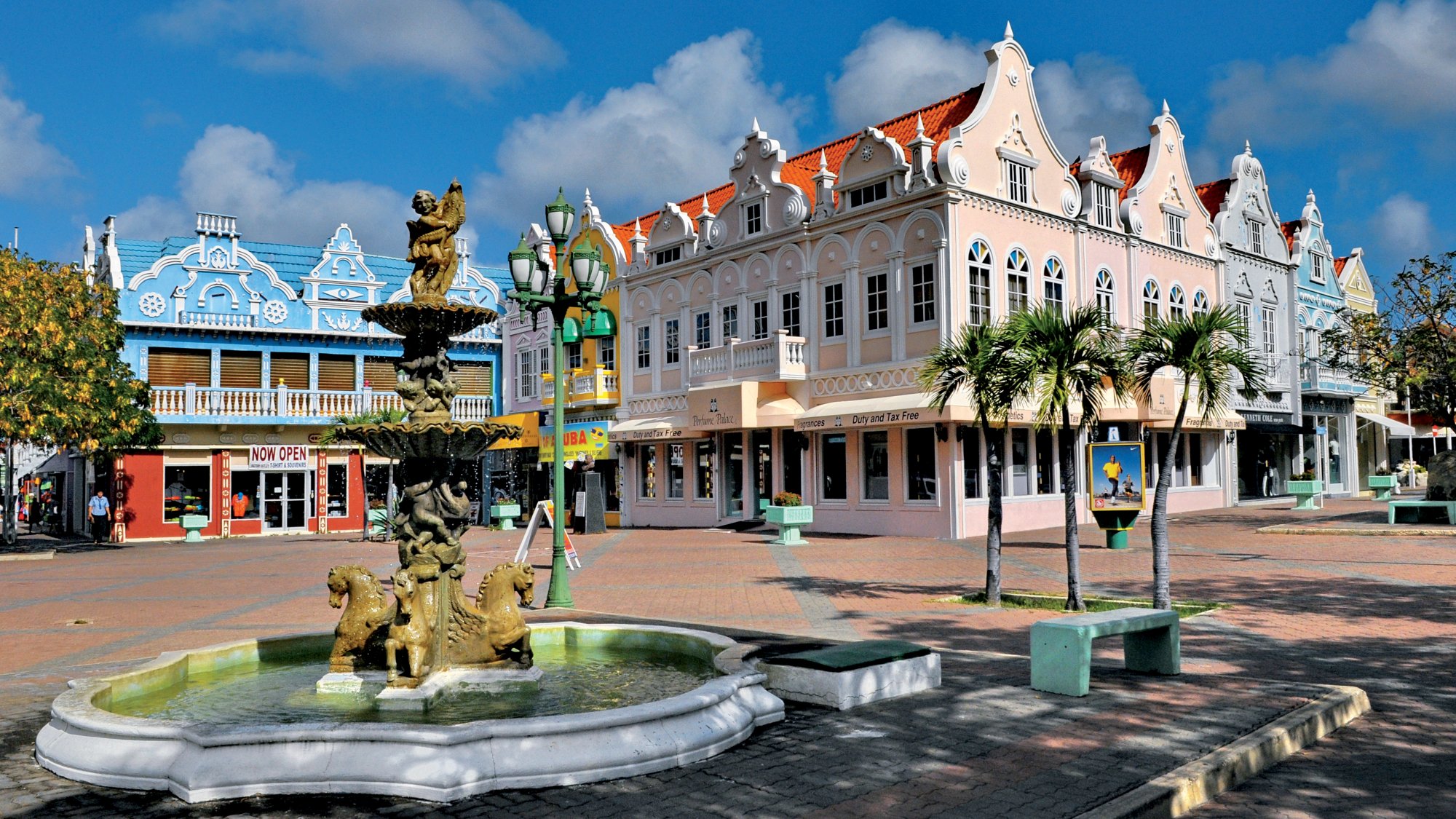 Bunte Kolonialgebäude mit Brunnen und Palmen auf einem sonnigen Platz.