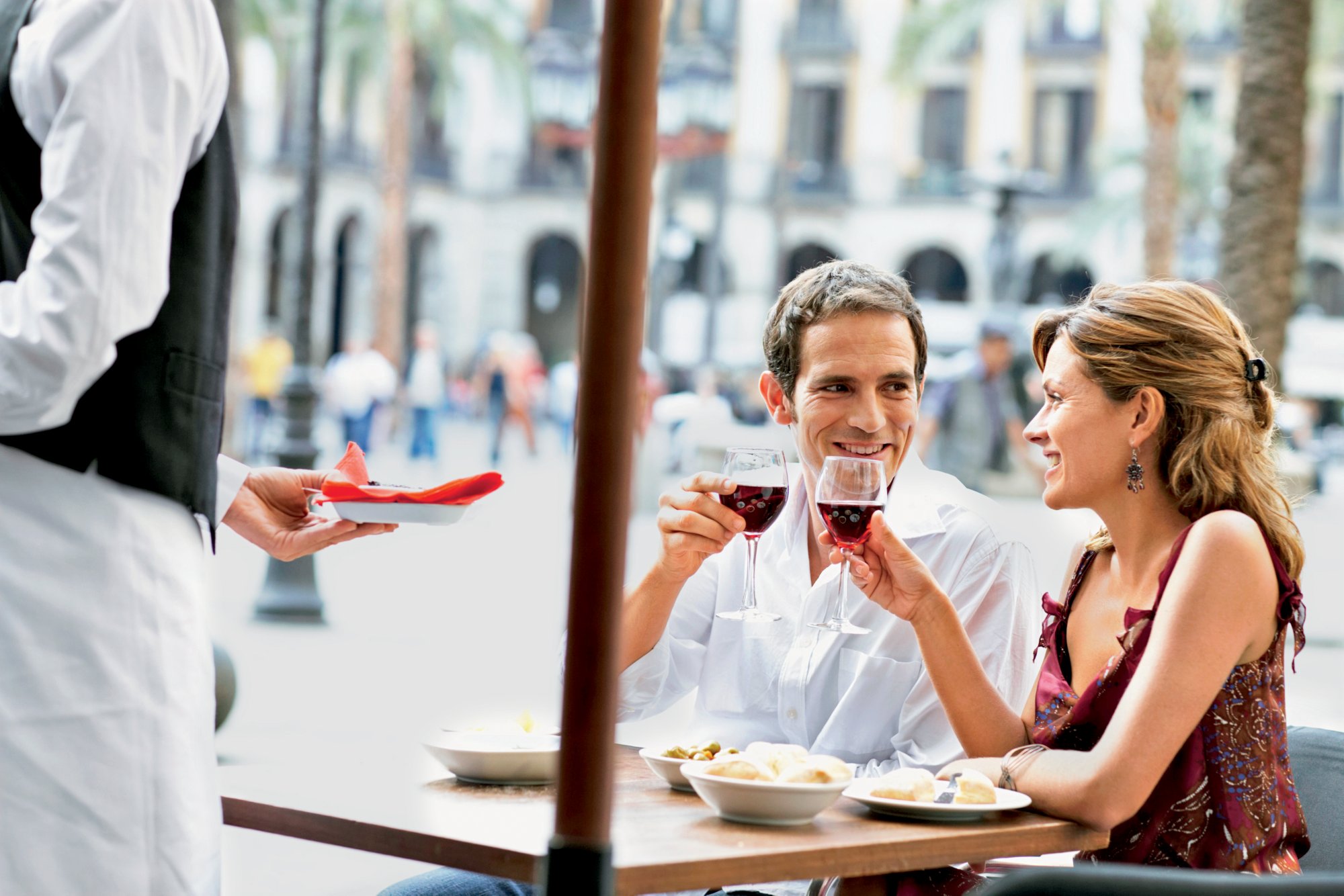 Spain, Barcelona, Placa Real, waiter serving couple at outdoor cafe