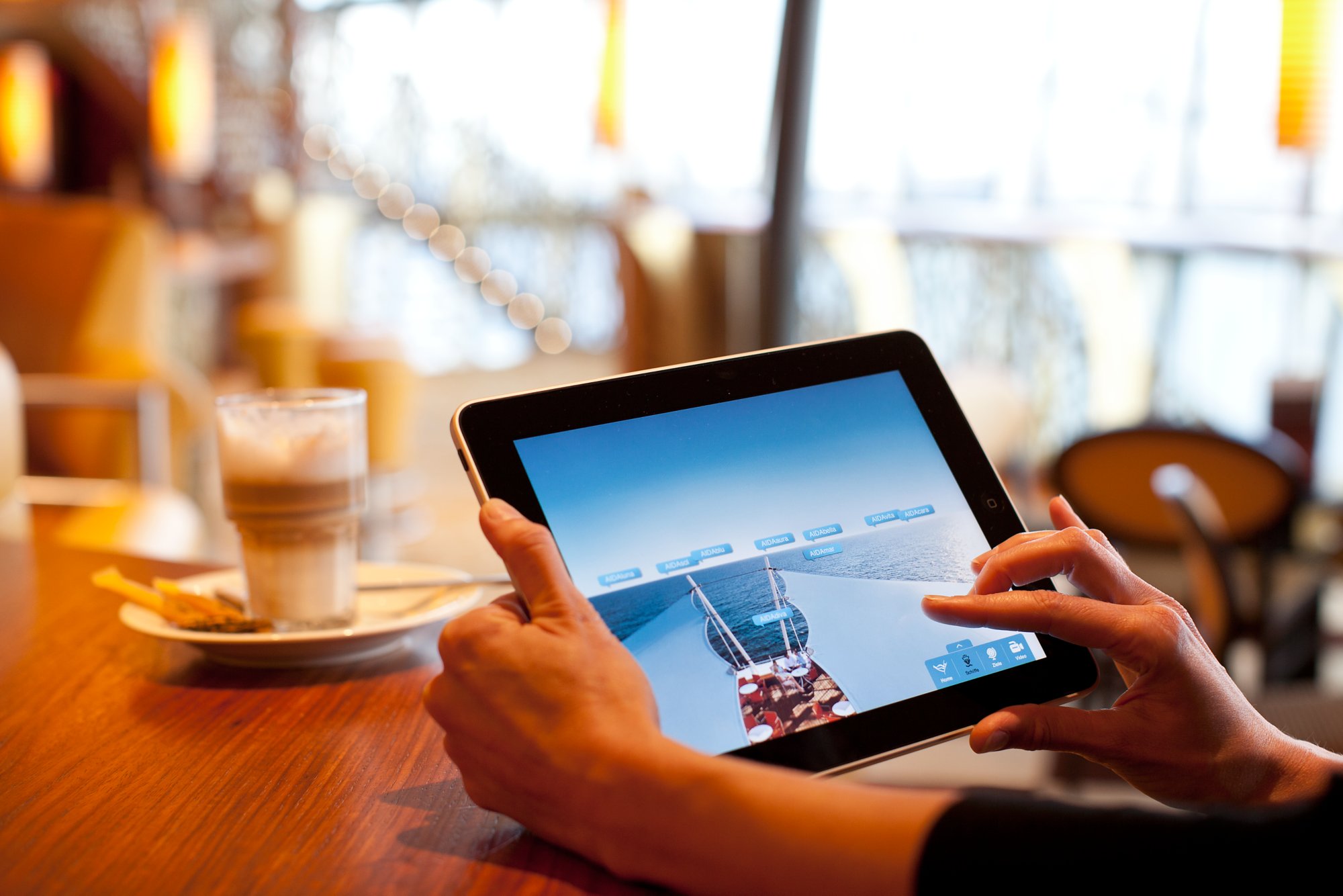 Tablet in der Hand von einer Frau, daneben ein Kaffee