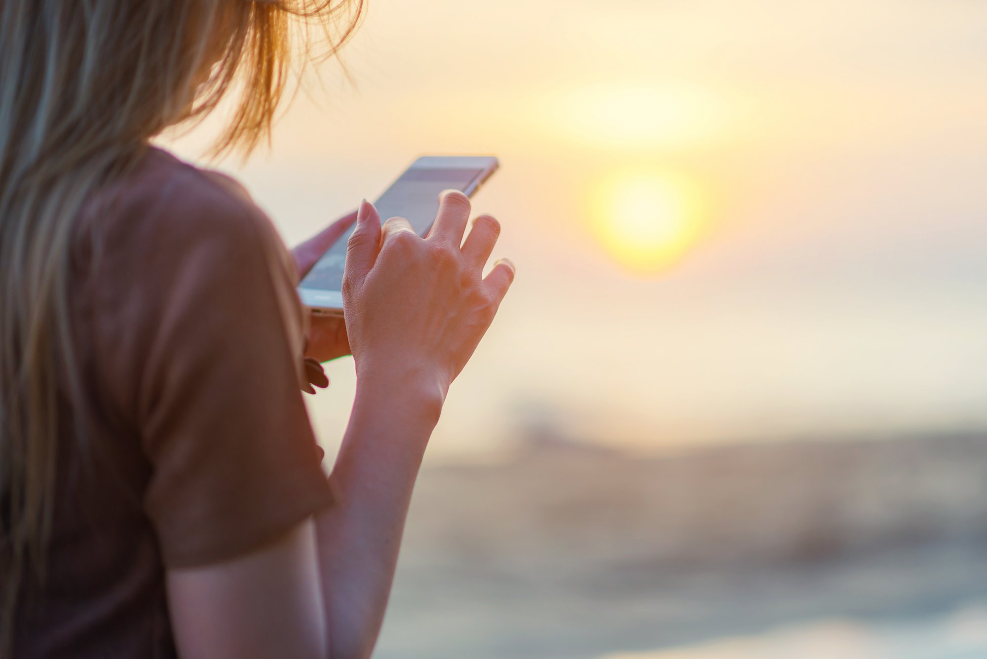 woman texting on smart phone on the beach during sunset; Shutterstock ID 565493335; Purchase Order: -