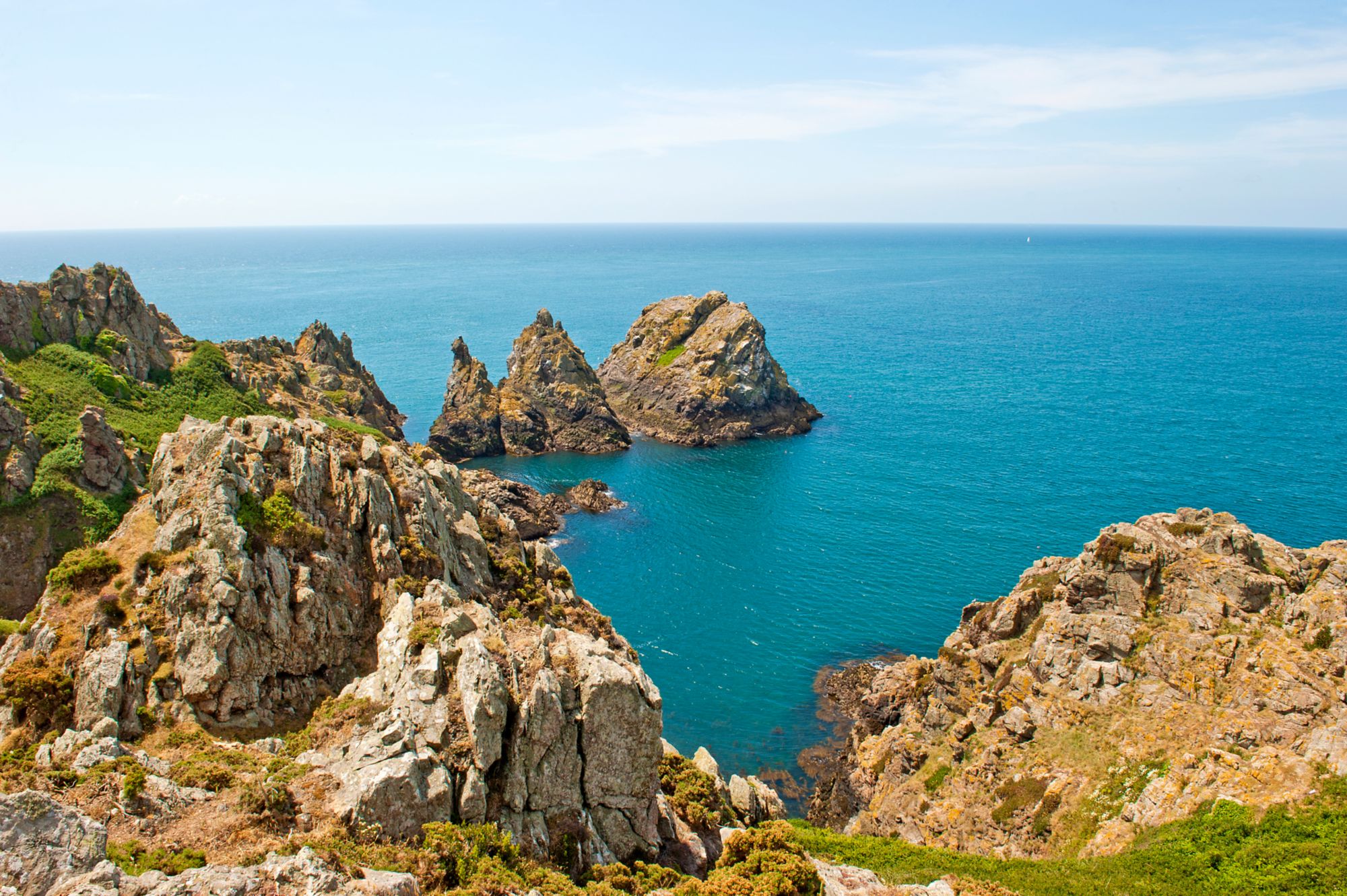Unberührte Küstenlandschaft auf Guernsey mit felsigen Klippen und klarem blauen Meer unter leicht bewölktem Himmel.