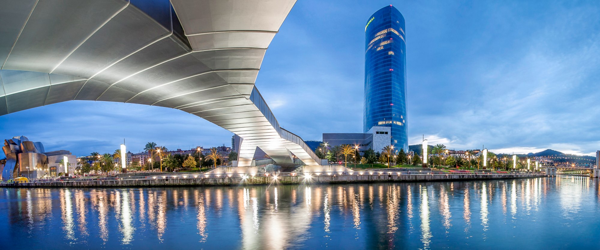 Panoramablick auf Bilbao mit modernem Brückendesign, Hochhaus und Flussreflexionen.