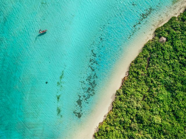 Küstenlandschaft bei Port Louis mit türkisfarbenem Meer, Sandstrand, grüner Vegetation und kleinem Boot nahe dem Ufer.