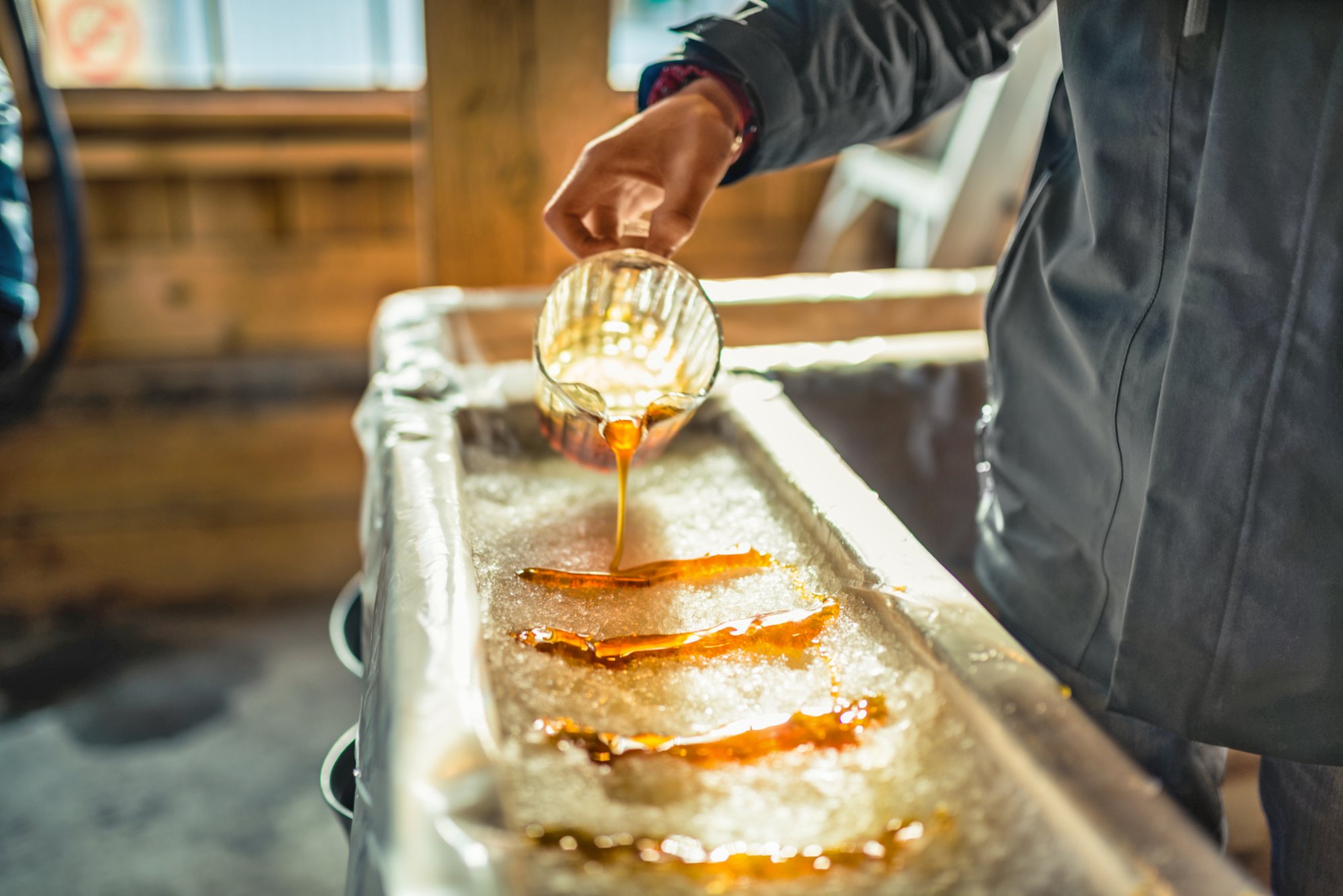 A close-up of a person at sugar shack pouring maple syrup onto snow to make maple sugar taffy