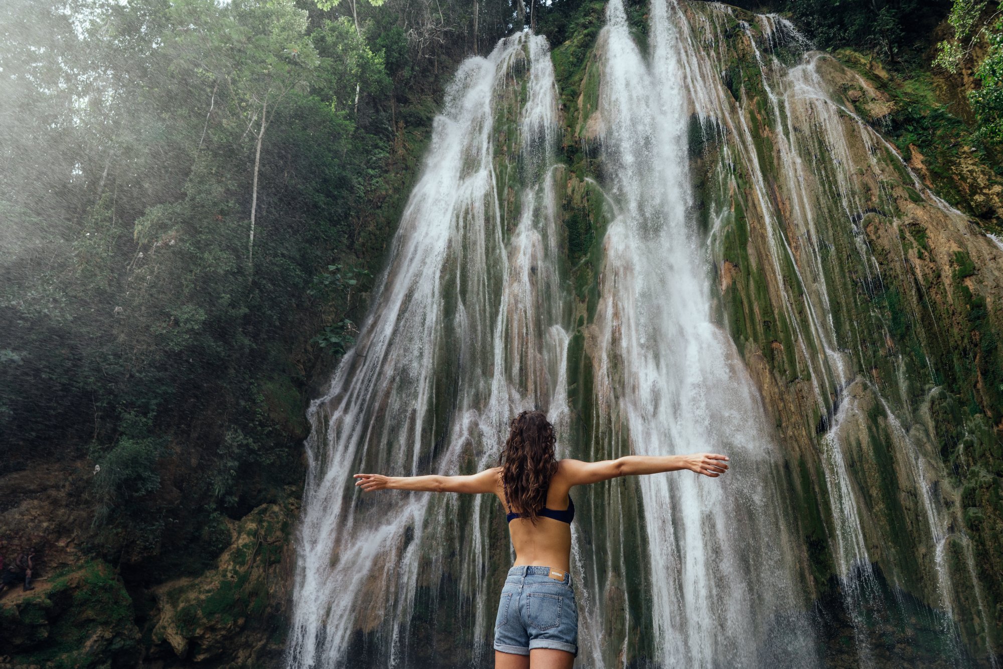 Frau steht mit geöffneten Armen vor einem Wasserfall