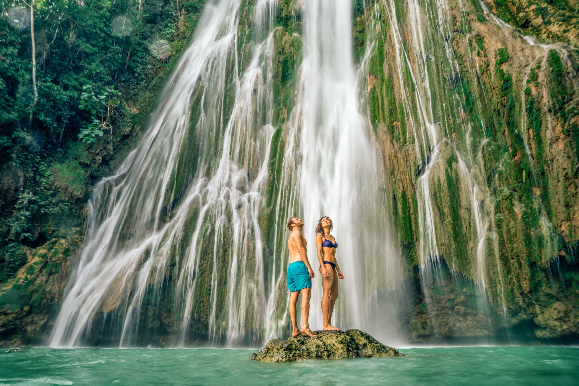 Ein Paar steht auf einem Stein im wasser und bewundert den Wasserfall El Limón in der Dominikanischen Republik