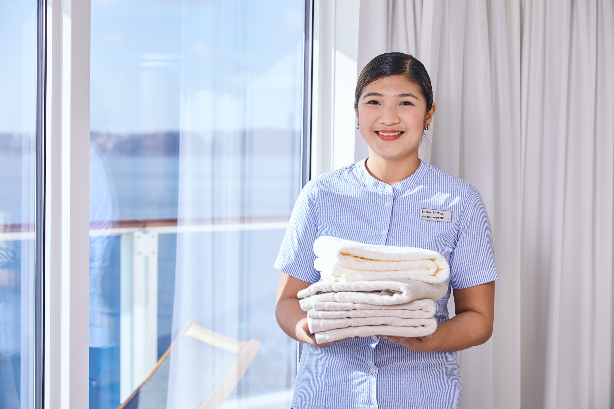 Housekeeping-Mitarbeiterin trägt einen Stapel Handtücher