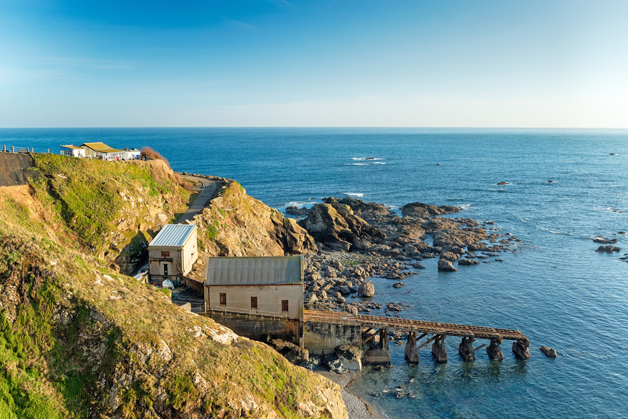 Küstenlandschaft in Falmouth, Cornwall mit Klippen, Gebäuden am Meer und einem Holzsteg ins klare Wasser.