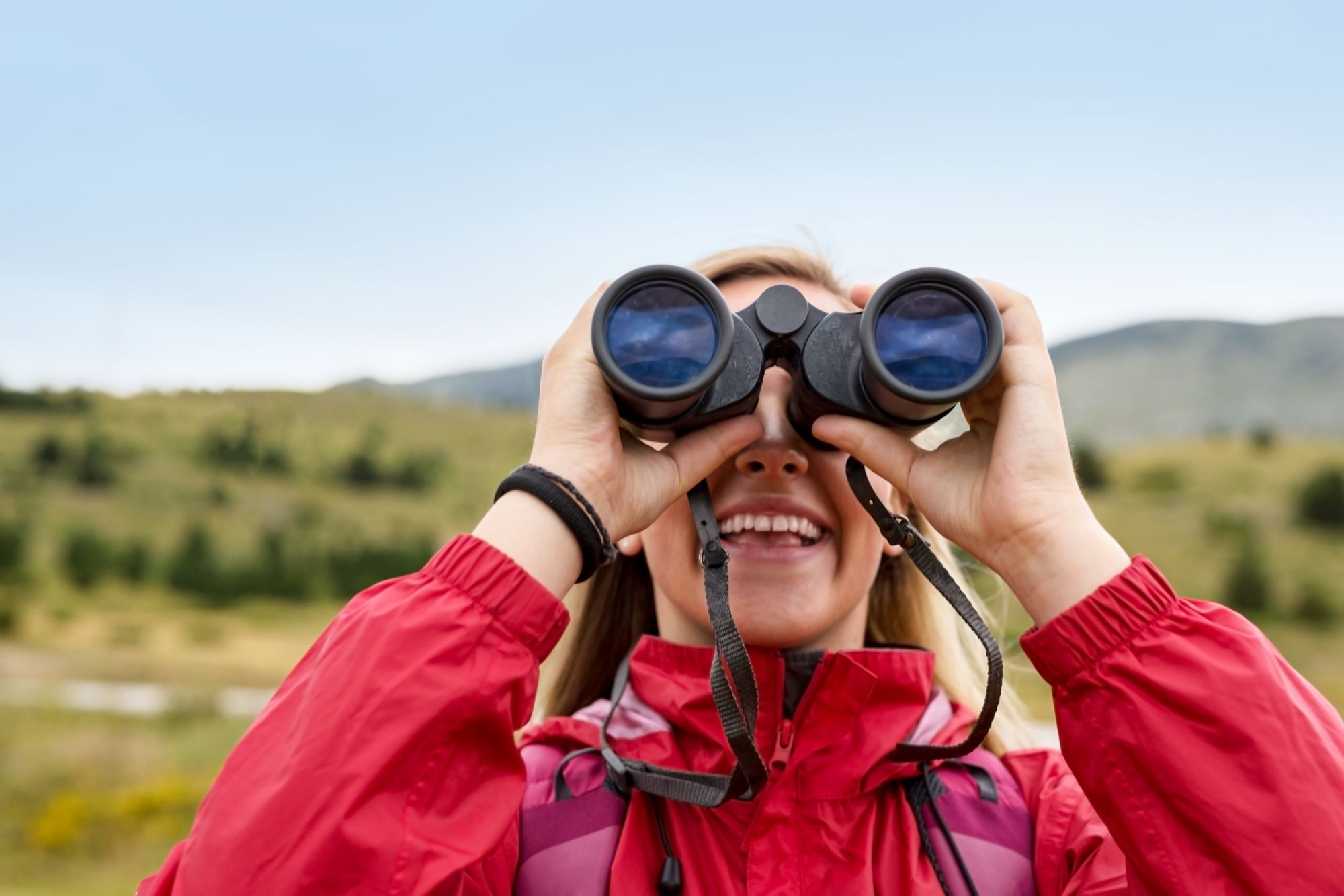 young blonde woman hiking and watching through binoculars.