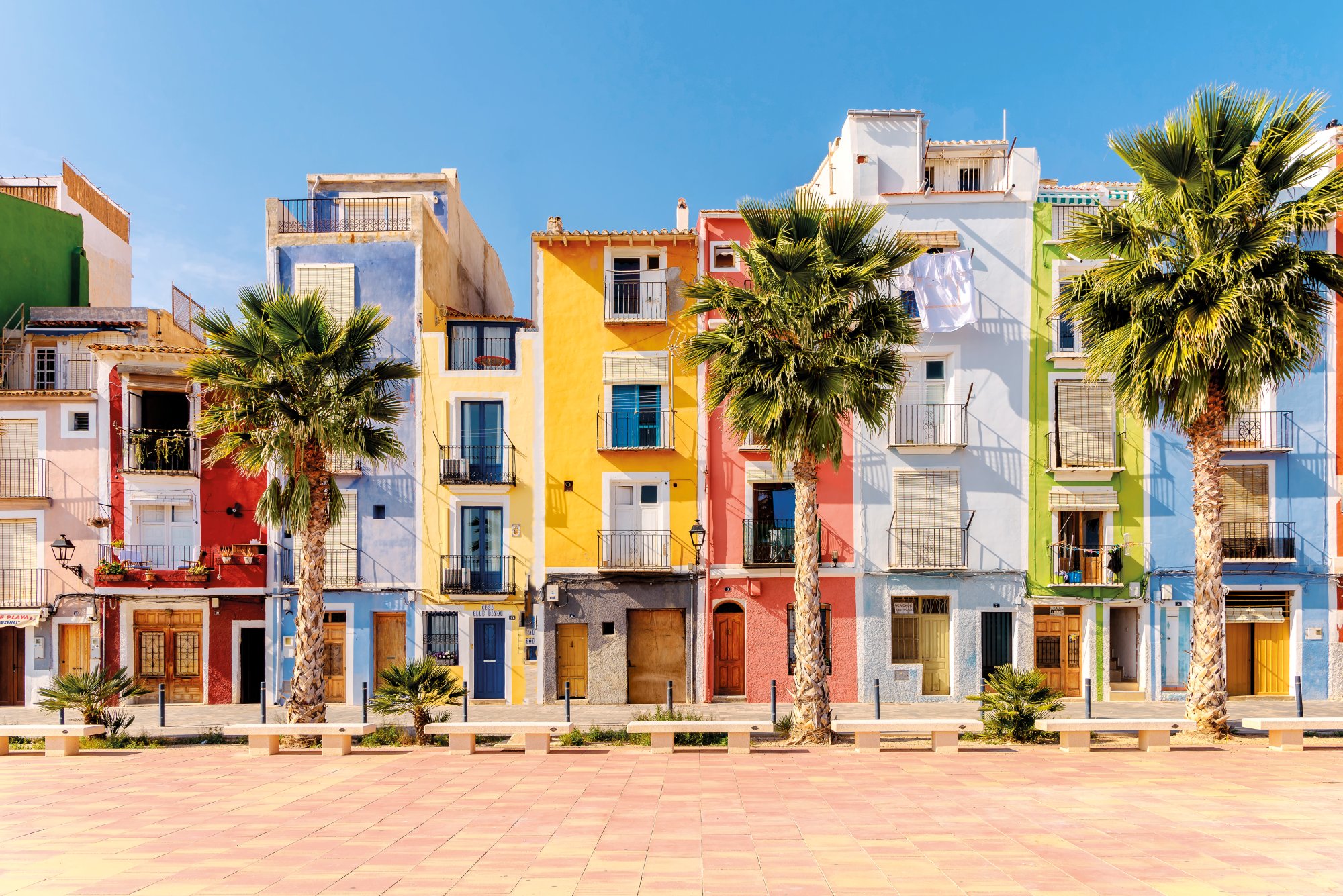 Bunte Häuserfassaden und Palmen in Alicante bei strahlend blauem Himmel.