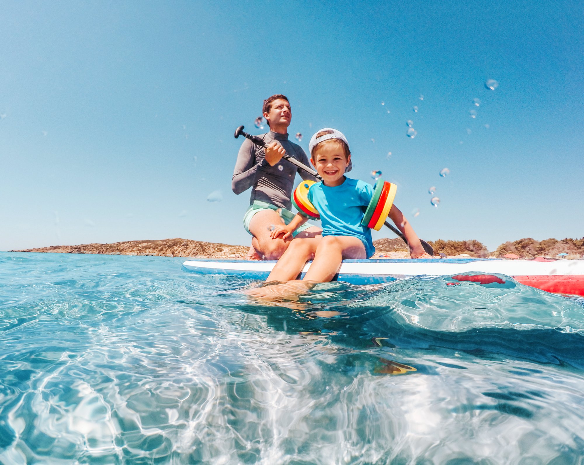 Photo of a cheerful little boy enjoys paddle boarding with his father