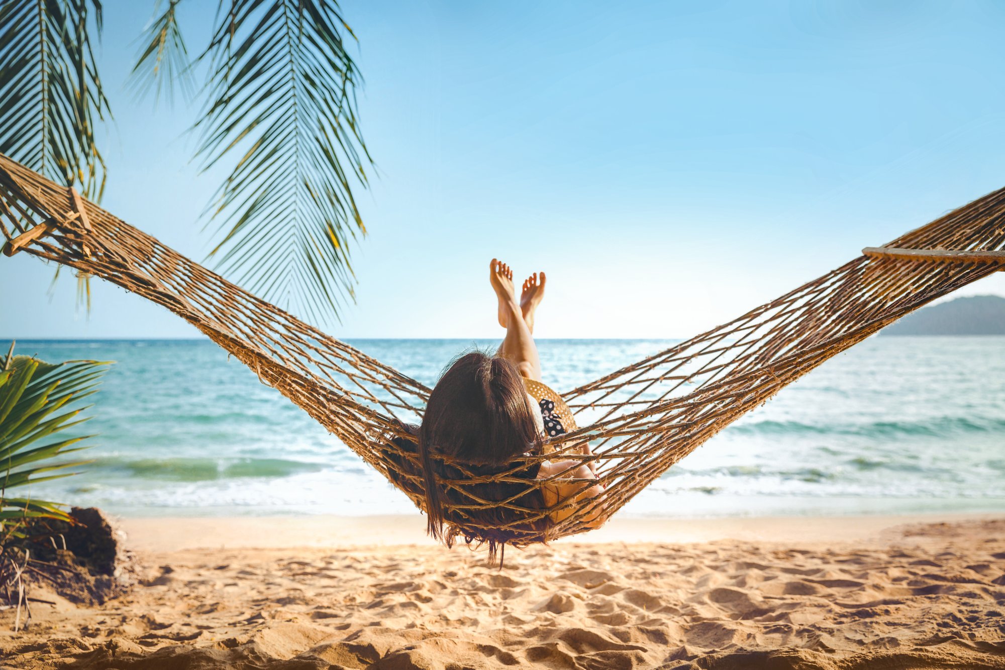 Summer vacations concept, Happy woman with white bikini, hat and shorts Jeans relaxing in hammock on tropical beach at sunset, Koh mak, Thailand