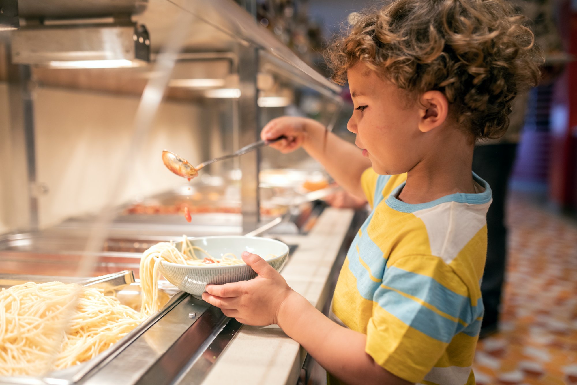 Kind füllt sich am Buffet Nudeln und Tomatensoße auf einen Teller