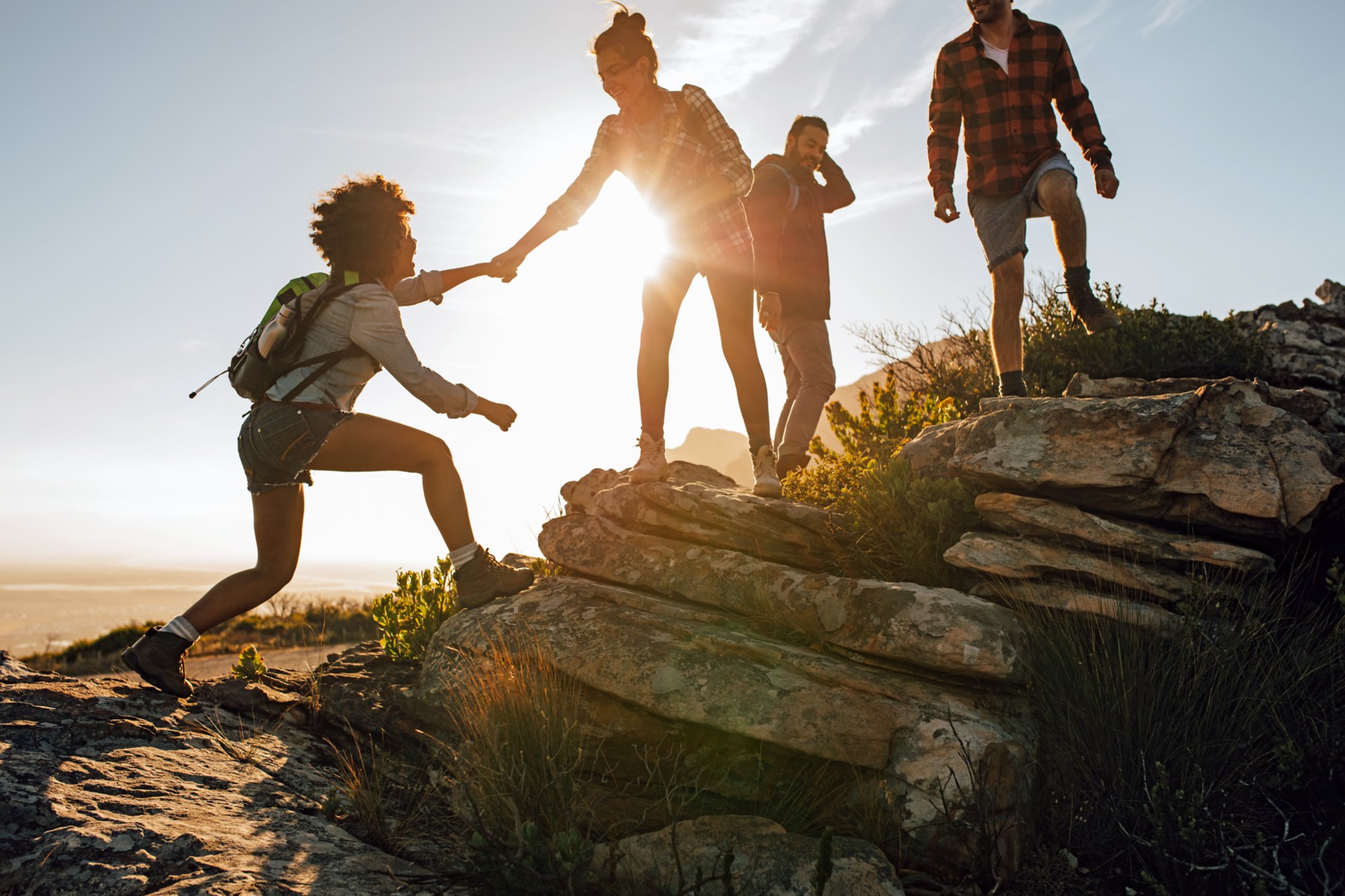 Group of hikers on a mountain. Woman helping her friend to climb a rock. Young people on mountain hike at sunset.