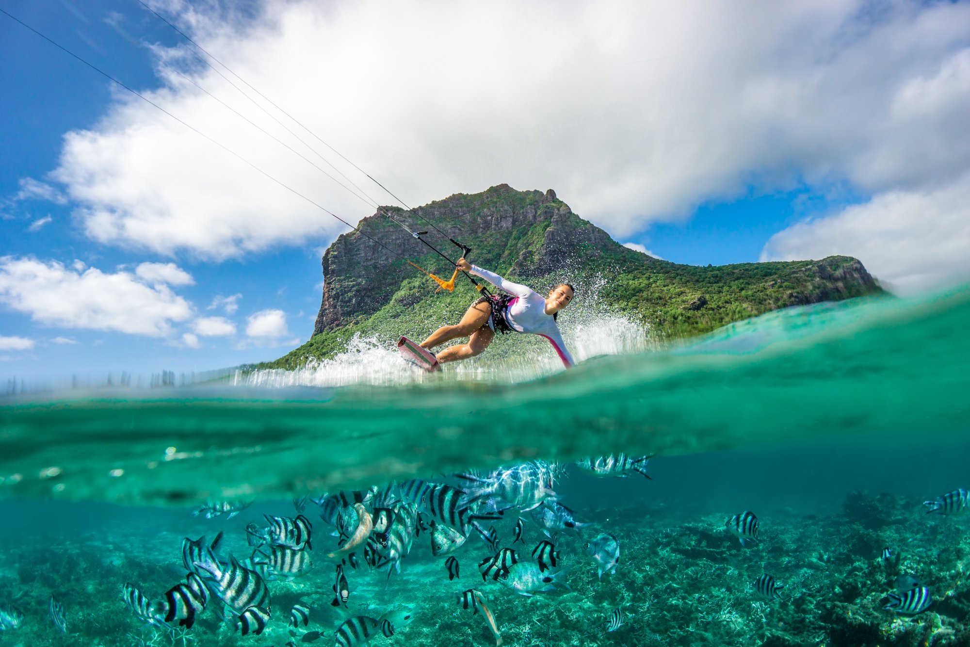 Beautiful girl with black hair kiting in the clear waters of the Indian Ocean in Mauritius on the background of clouds and high mountains. The lower part of the picture - the underwater world with fishes