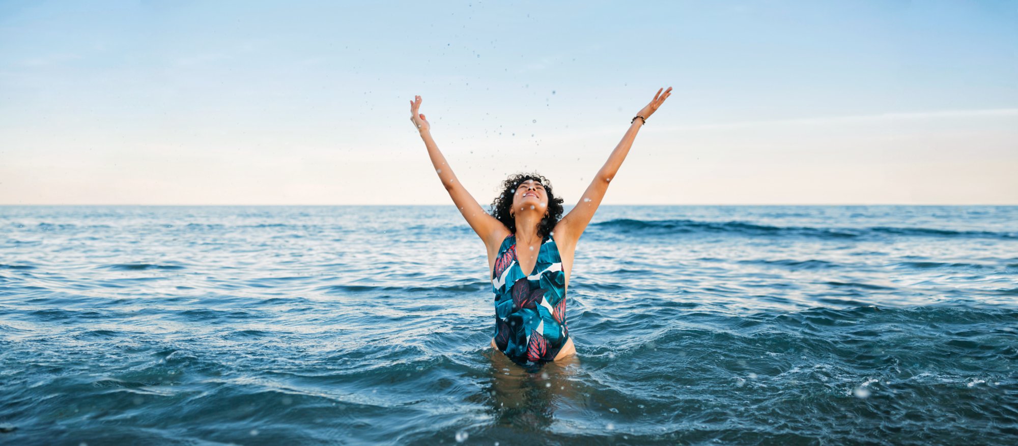 Junge Frau im Wasser spritzt mit Wasser in die Luft