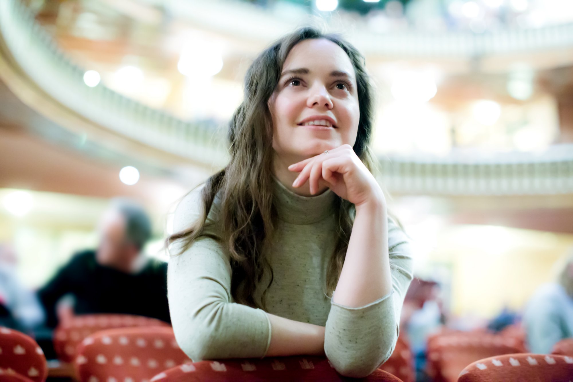 Portrait of positive woman sitting in theatre salon and watching show 