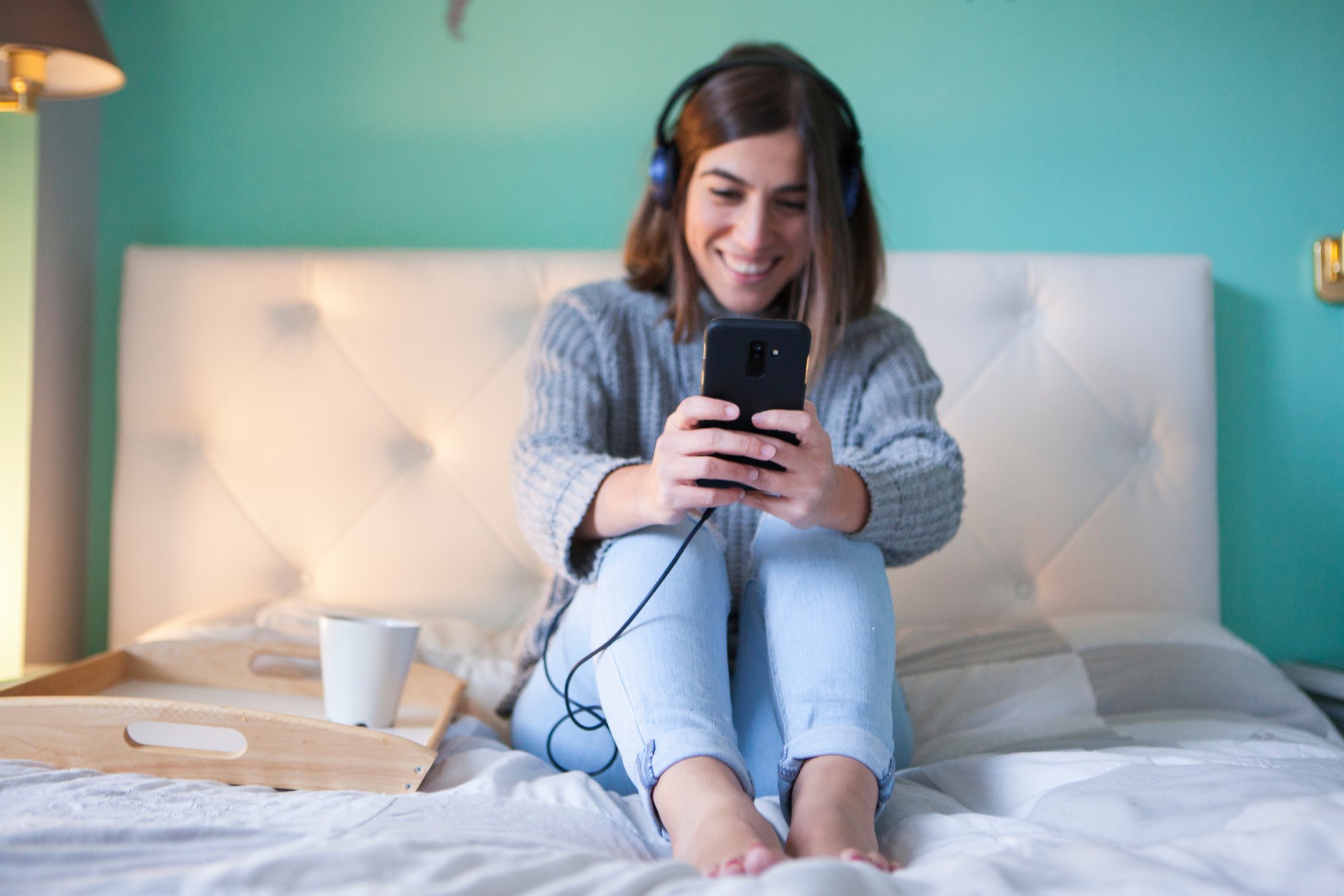 Frau sitzt auf dem Bett mit Smartphone in der Hand und freut sich