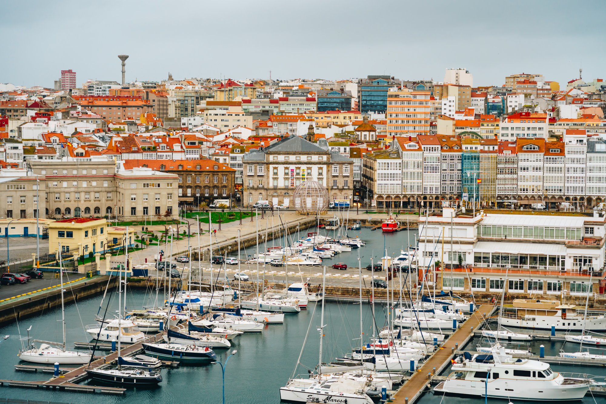 Yachthafen in A Coruña, Spanien, umgeben von farbigen Wohn- und Geschäftsgebäuden mit Blick auf die dicht bebaute Stadt im Hintergrund.
