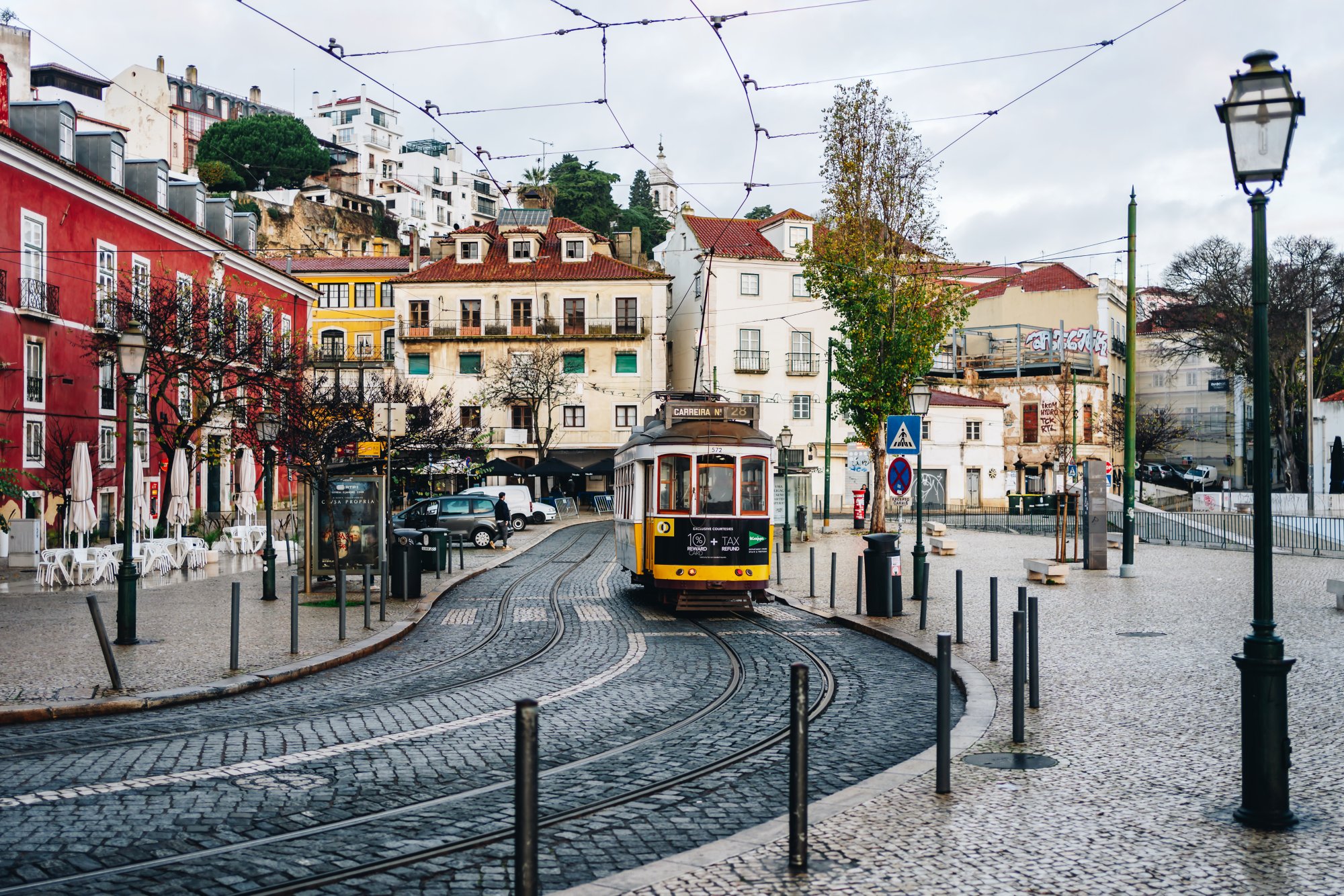 Straßenszene in Lissabon mit gelber Straßenbahn, bunten Häusern und Kopfsteinpflaster.