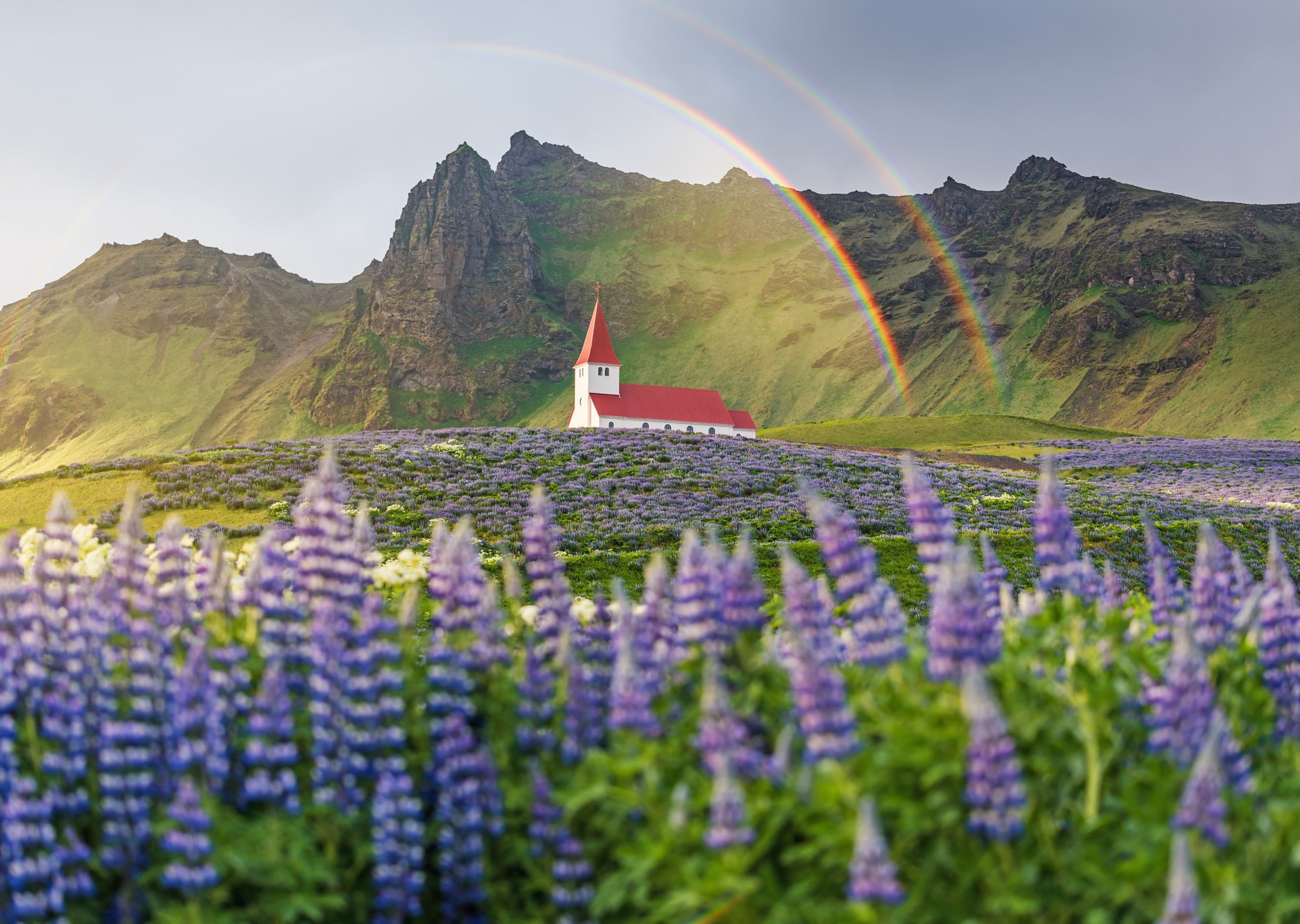 Blick auf Kirche vor Bergen mit zwei regenbögen