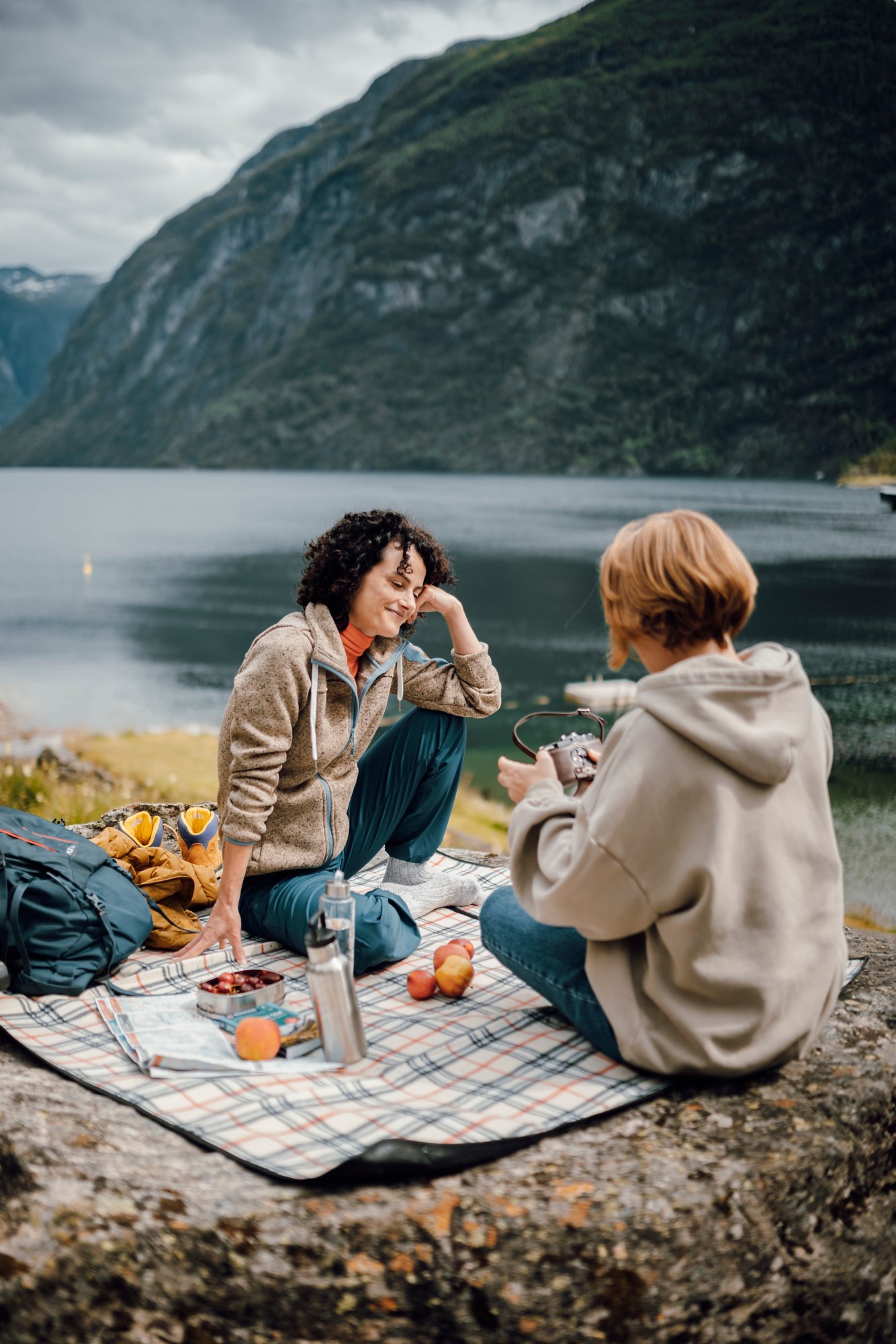 Zwei Frauen sitzen auf einer Decke beim Picknick an einem Fjord