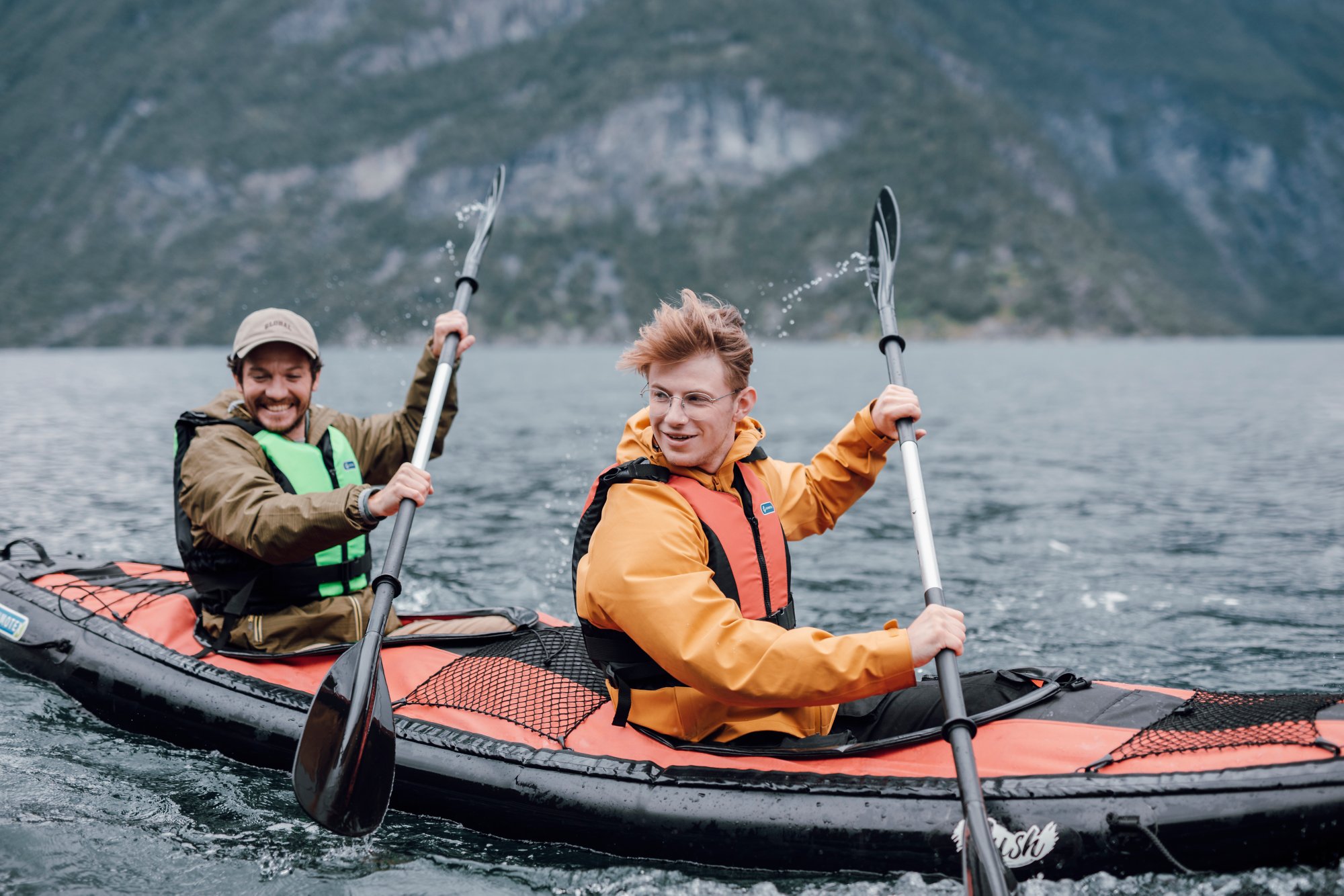 Zwei Männer fahren in einem Kajak vor einer Bergkulisse