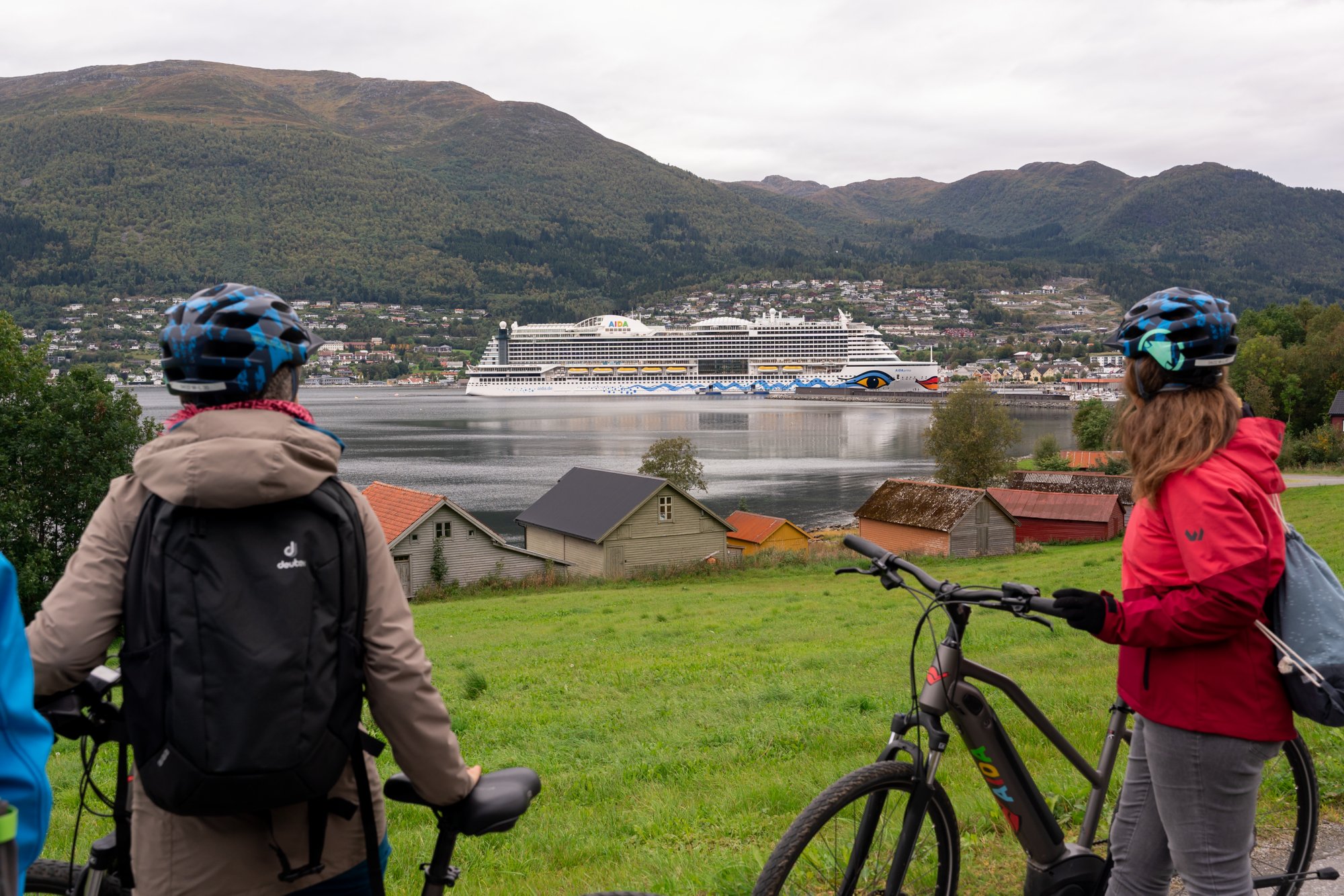 Zwei Fahrradfahrer blicken auf AIDAprima die im Hafen von Nordfjordeid liegt Nordfjordeid