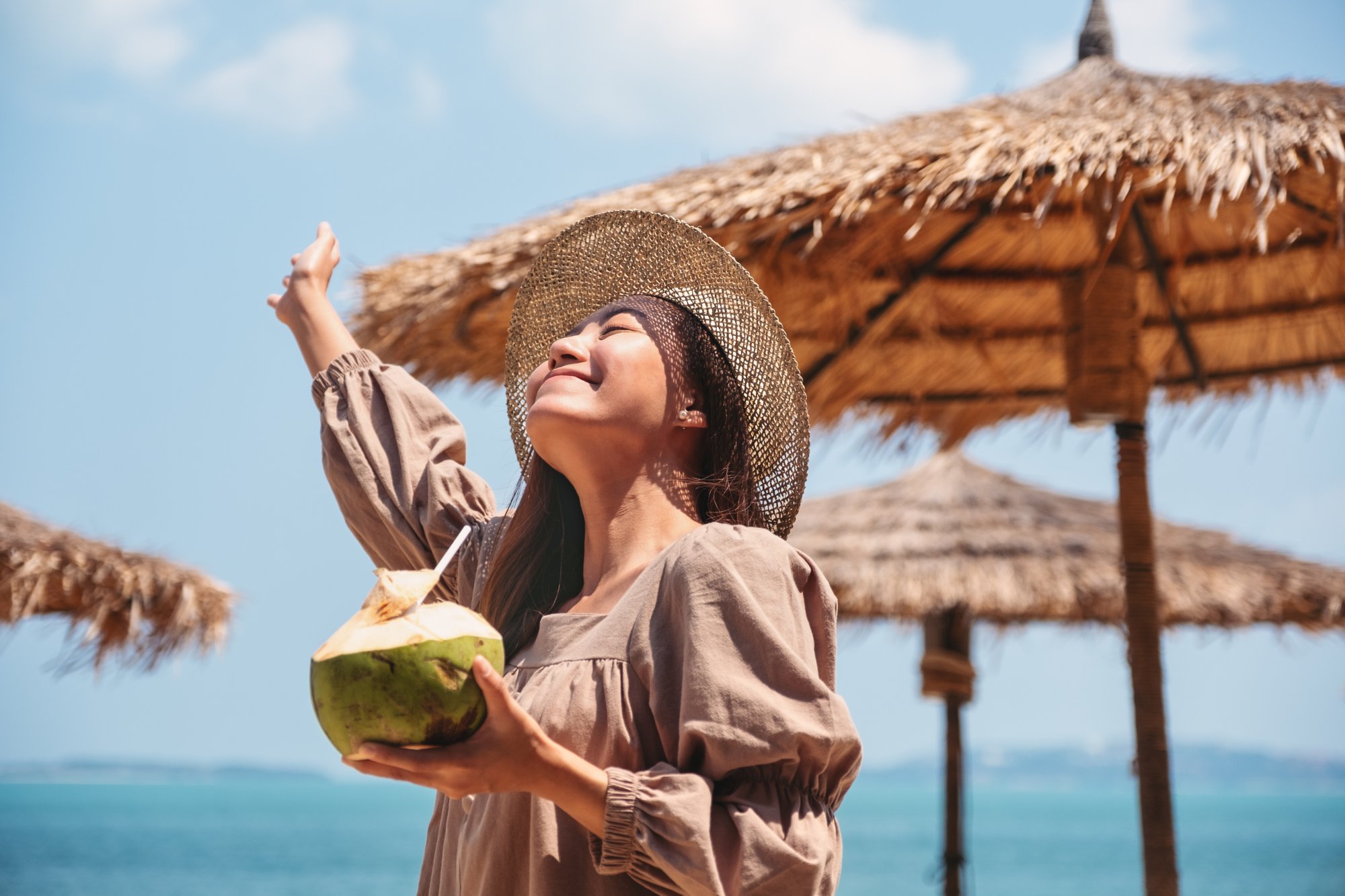 Portrait image of a beautiful asian woman holding a fresh coconut and enjoying on the beach